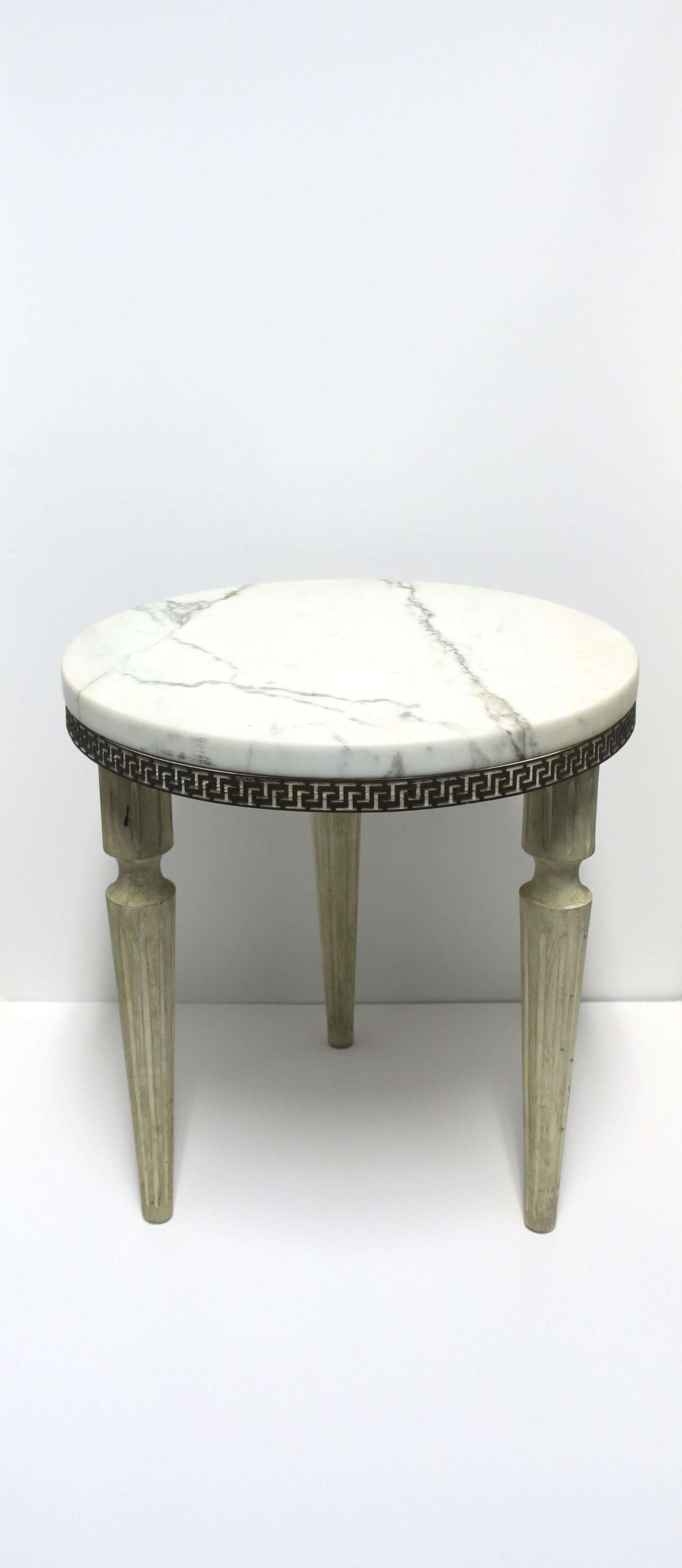 A white and dark veining marble side drinks table in the Neoclassical style, circa mid-20th century. Table is round with a substantial Carrara marble top, Greek-Key metal decorative edge, and fluted legs. Base is white wood with an antique finish on