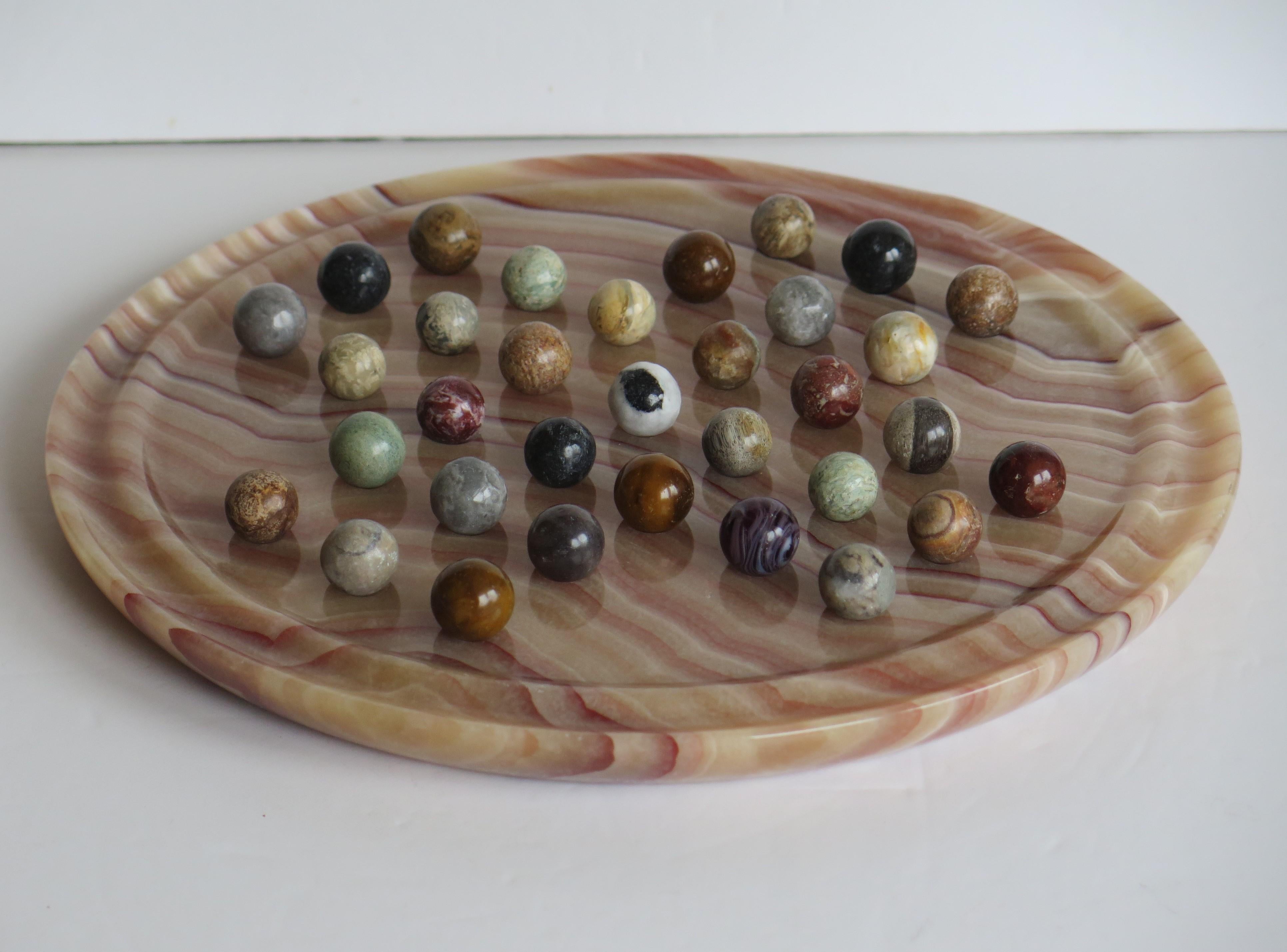 This is a complete board game of marble solitaire with a beautiful marble stone board and 33 agate mineral stone marbles all dating to the mid-20th century.

The board is very attractive and unusual being made of a heavy stone material with a fine
