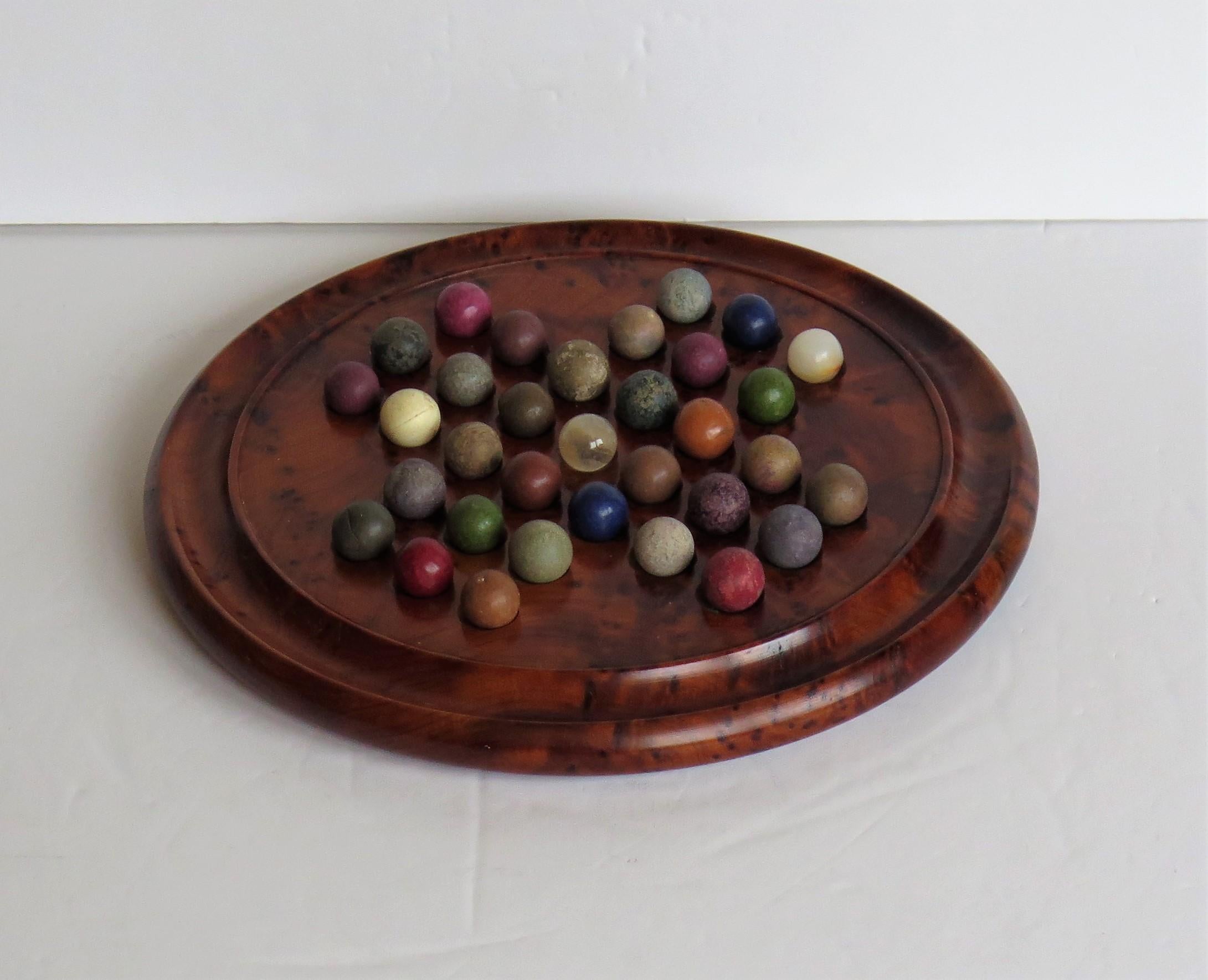 This is a complete board game of marble solitaire from the late 19th century.

The circular turned board is very attractive being made of a burr wood, possibly Maple, with a gallery to the outer perimeter. The board has 32 equi-spaced holes with
