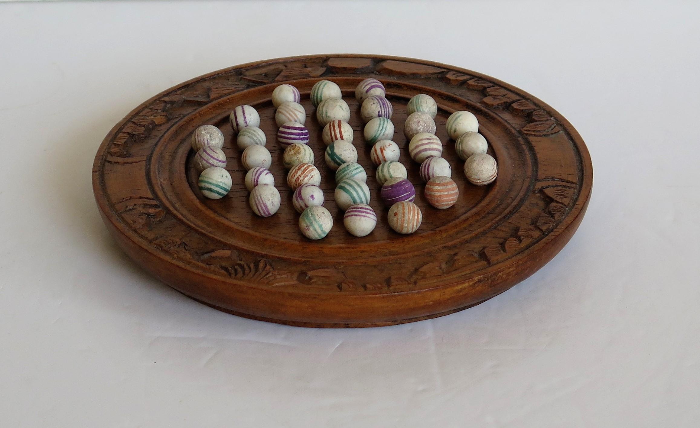 This is a complete board game of marble solitaire from the second half of the 19th century.

The small diameter 6.5 inch circular turned board is very attractive being made of a hardwood, possibly Walnut, with a gallery to the outer perimeter and