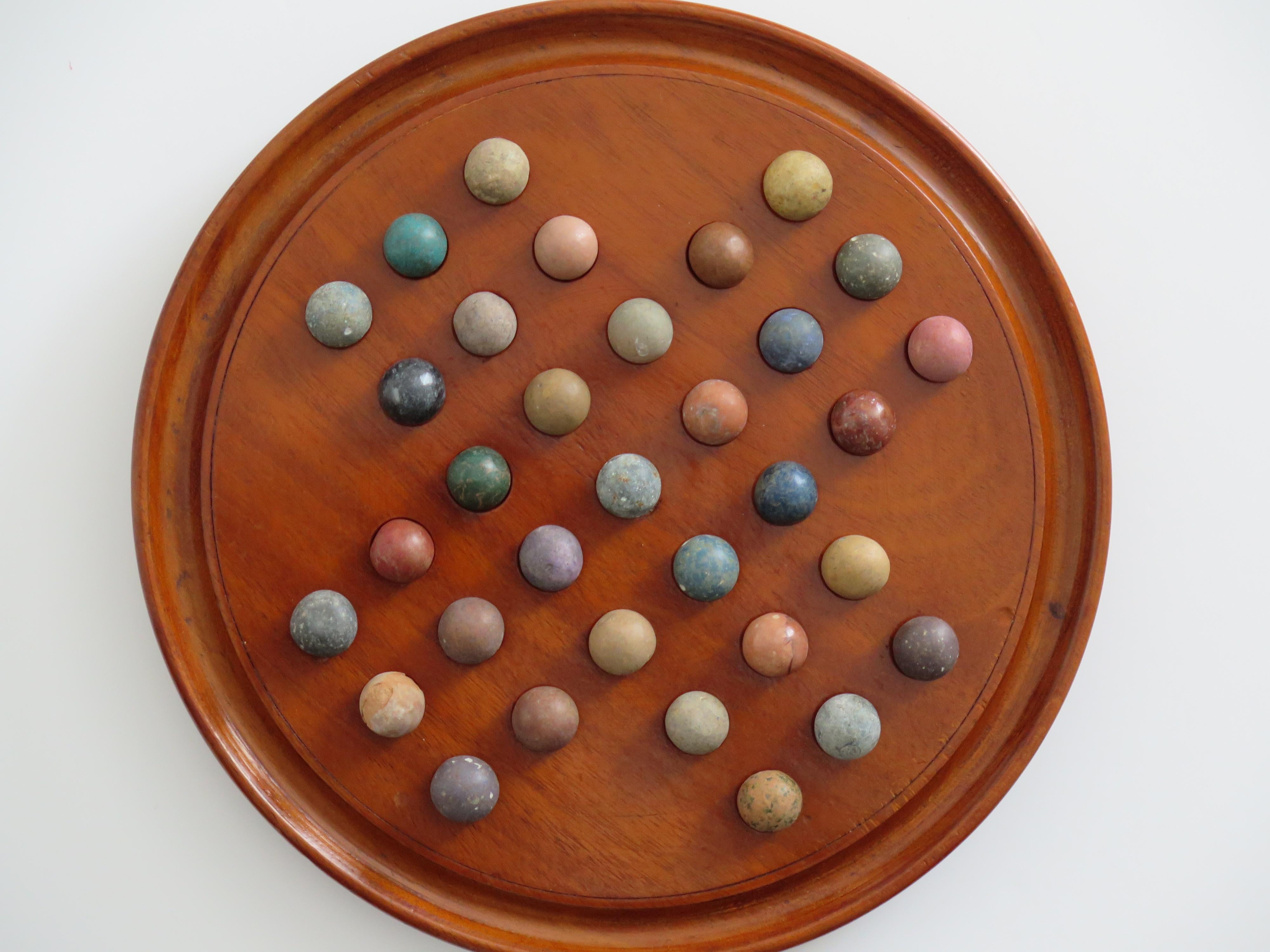This is a complete game of Marble Solitaire with a very good polished hand turned hardwood board and 33 early clay and stone marbles, all dating to the 19th century, Victorian period.

The board is a fairly large size a 9.4 inch diameter and is