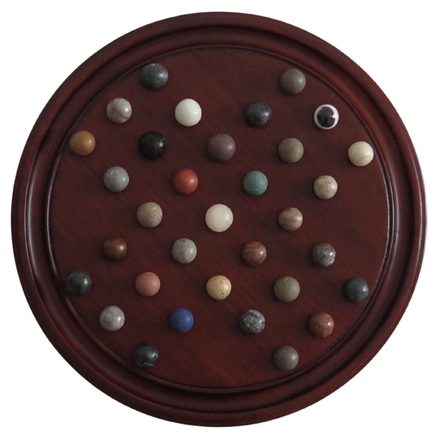 This is a very attractive complete game of Marble Solitaire with a hardwood circular board and 35 mixed stone marbles, probably French.

The circular turned board is made of polished hardwood, with a good grain figure. The board has 32 equi-spaced