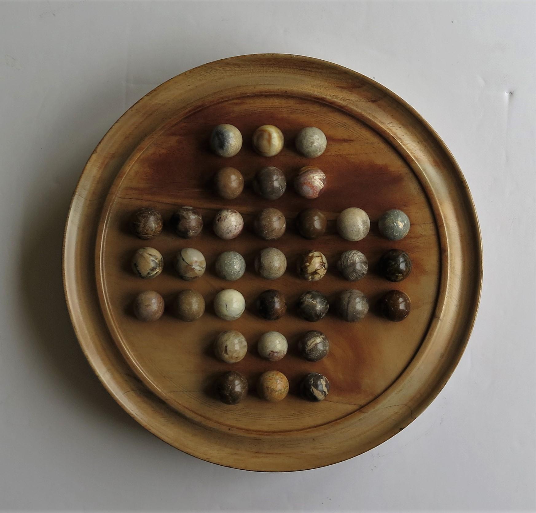 This is a very attractive complete game of Marble Solitaire with a hand turned hardwood board and 33 beautiful agate mineral stone marbles, probably French and all dating to the early 20th century, circa 1920.

The circular hand turned board is