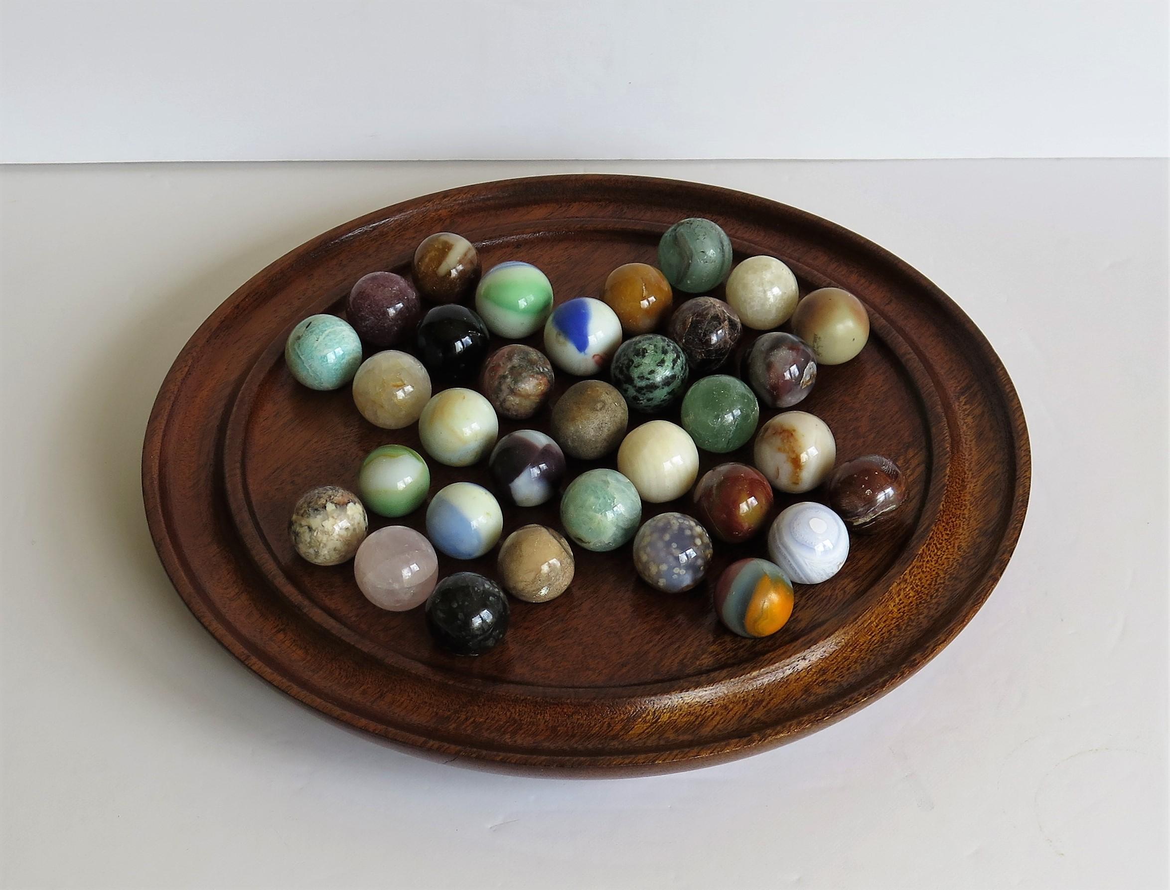 This is a very decorative and complete board game of 33 hole marble solitaire with a mid size hardwood board and 33 individual mainly mineral or agate stone and some glass marbles, which we date to the early 20th century, probably of French