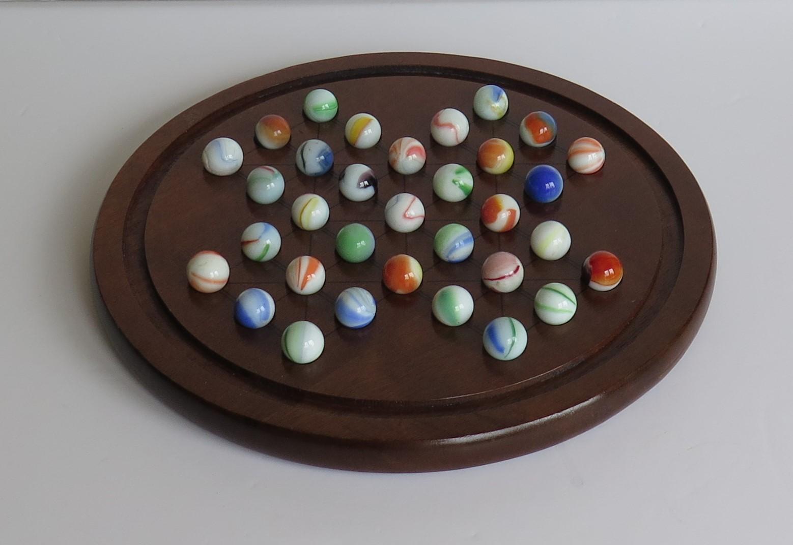 This is a good marble solitaire game, having a very good hardwood board and a complete set of 33 glass swirl marbles, all dating to the first half of the 20th century.

The circular turned board is made of hard-wood, possibly mahogany and has a