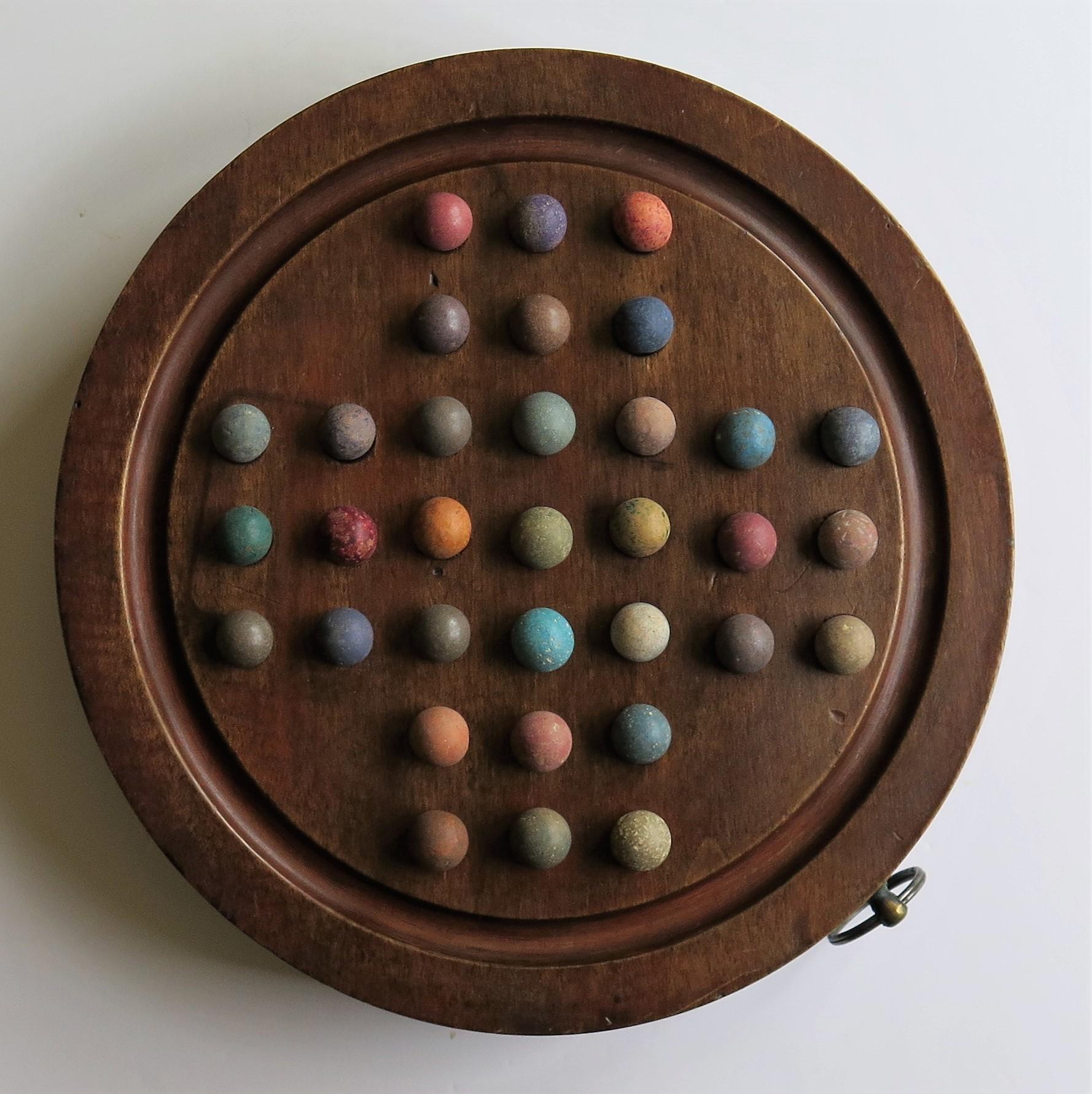 This is an original and complete game of Marble Solitaire with a heavy hardwood board and 33 early clay and stone marbles, all dating to the mid-19th century, Victorian period, or possibly earlier.

This is a substantial hand turned circular