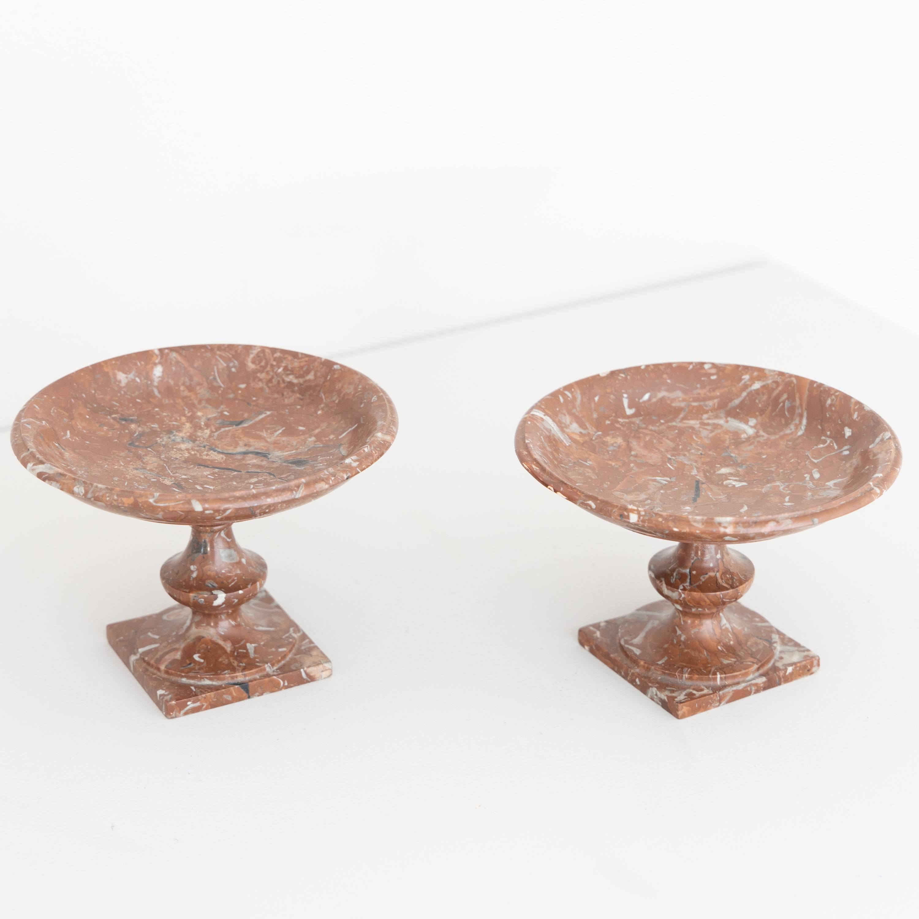 Two small red marble tazzas of slightly different design and height. Profiled vase-shaped shafts with shallow bowls rise above square plinths. One of the tazzas has an old restoration.