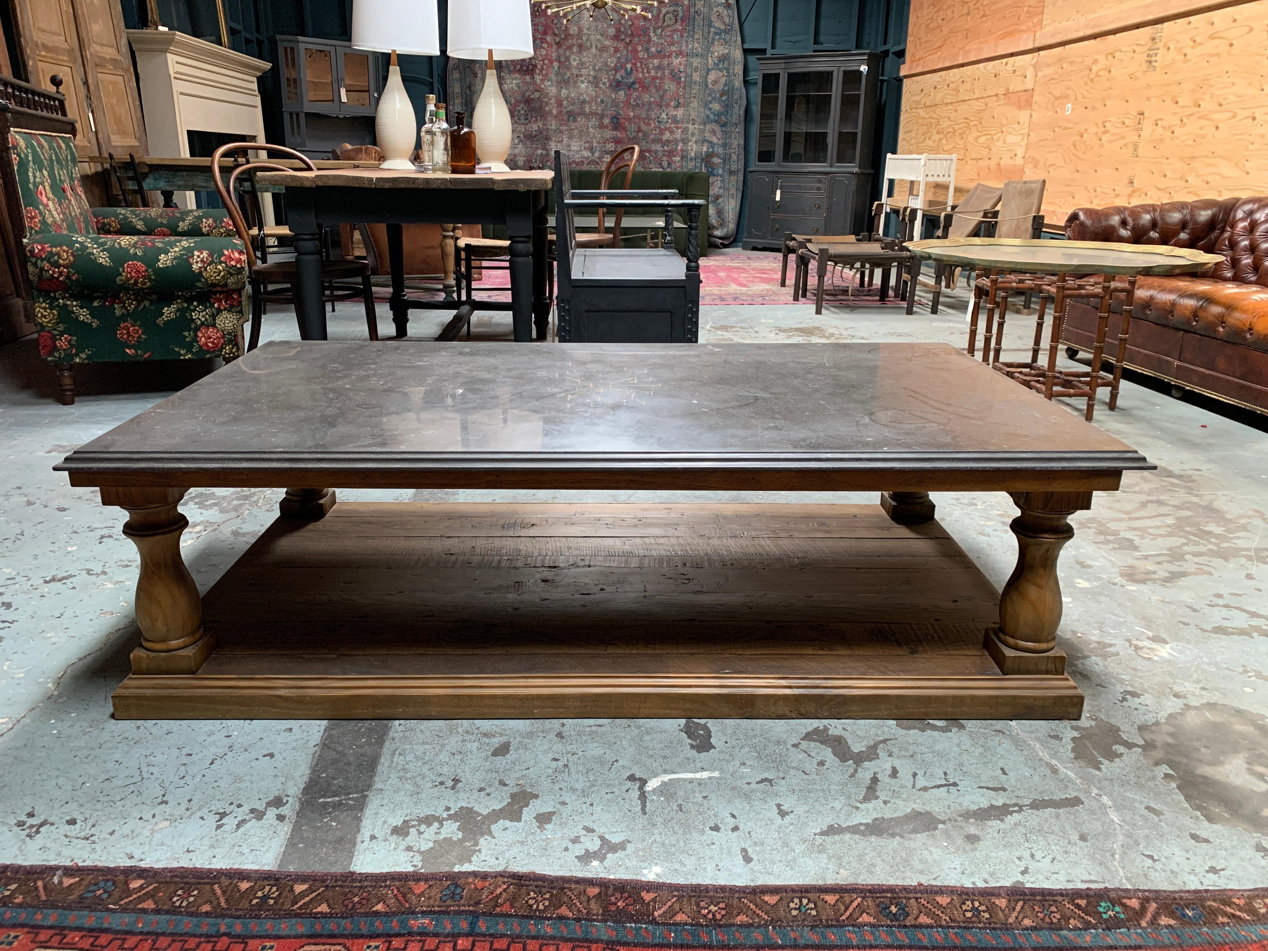 Dark marble-Top coffee table with a large footprint. Solid grey marble top with White veining sites atop a poster base, with wood top and bottom, and thick turned legs to support the weight and majesty of the marble. 

Table is in great condition,