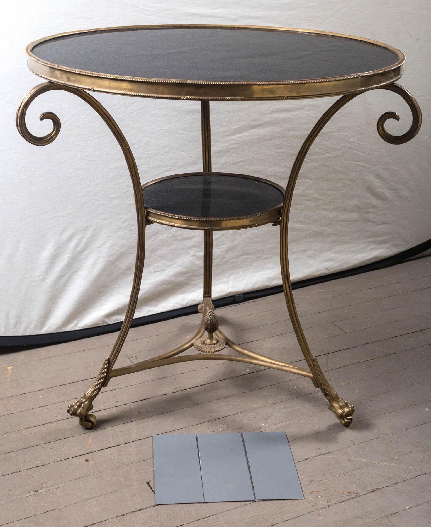 Made of solid brass with a black marble top and lower marble round, this table is in the Directoire style.
Gadrooned edge, dramatic scrolling legs, tripartite stretcher topped by an acorn finial. Brass casters below paw feet.