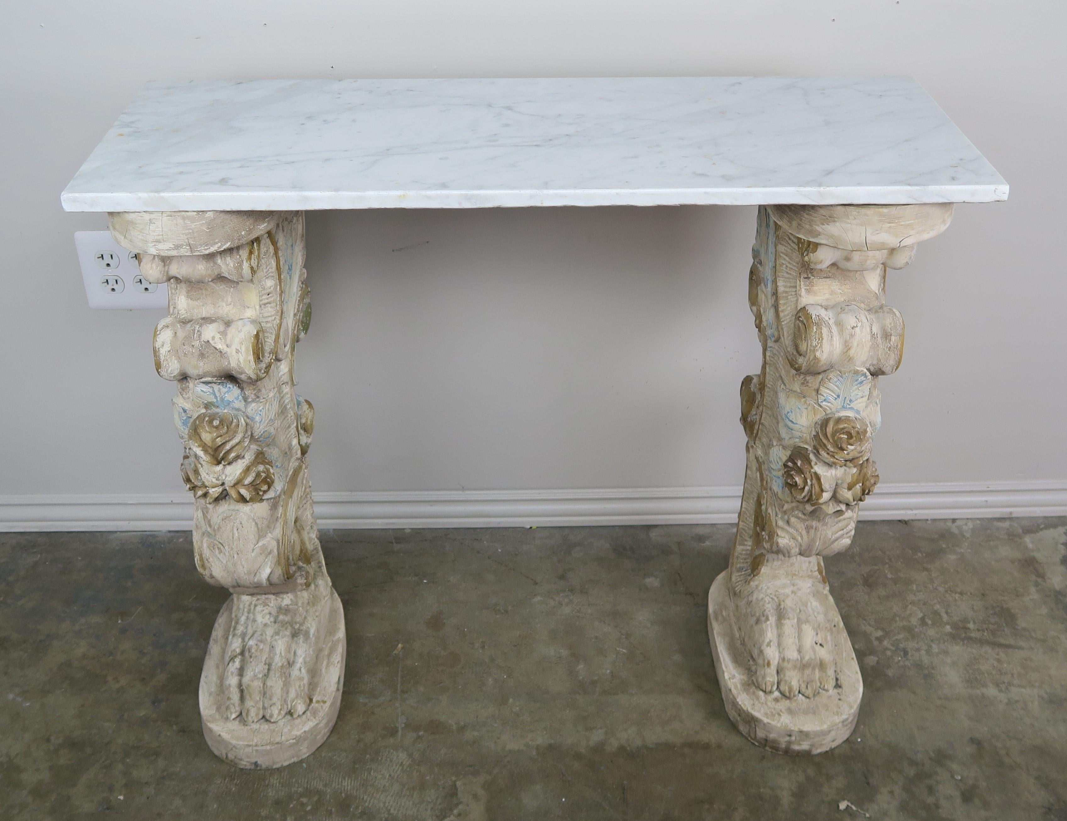 Marble-top console that consists of a Carrara marble top that sits on a pair of Italian carved wood pedestals with paw feet. The pedestals also have intricate carved roses along with scrolls and acanthus leaves throughout.