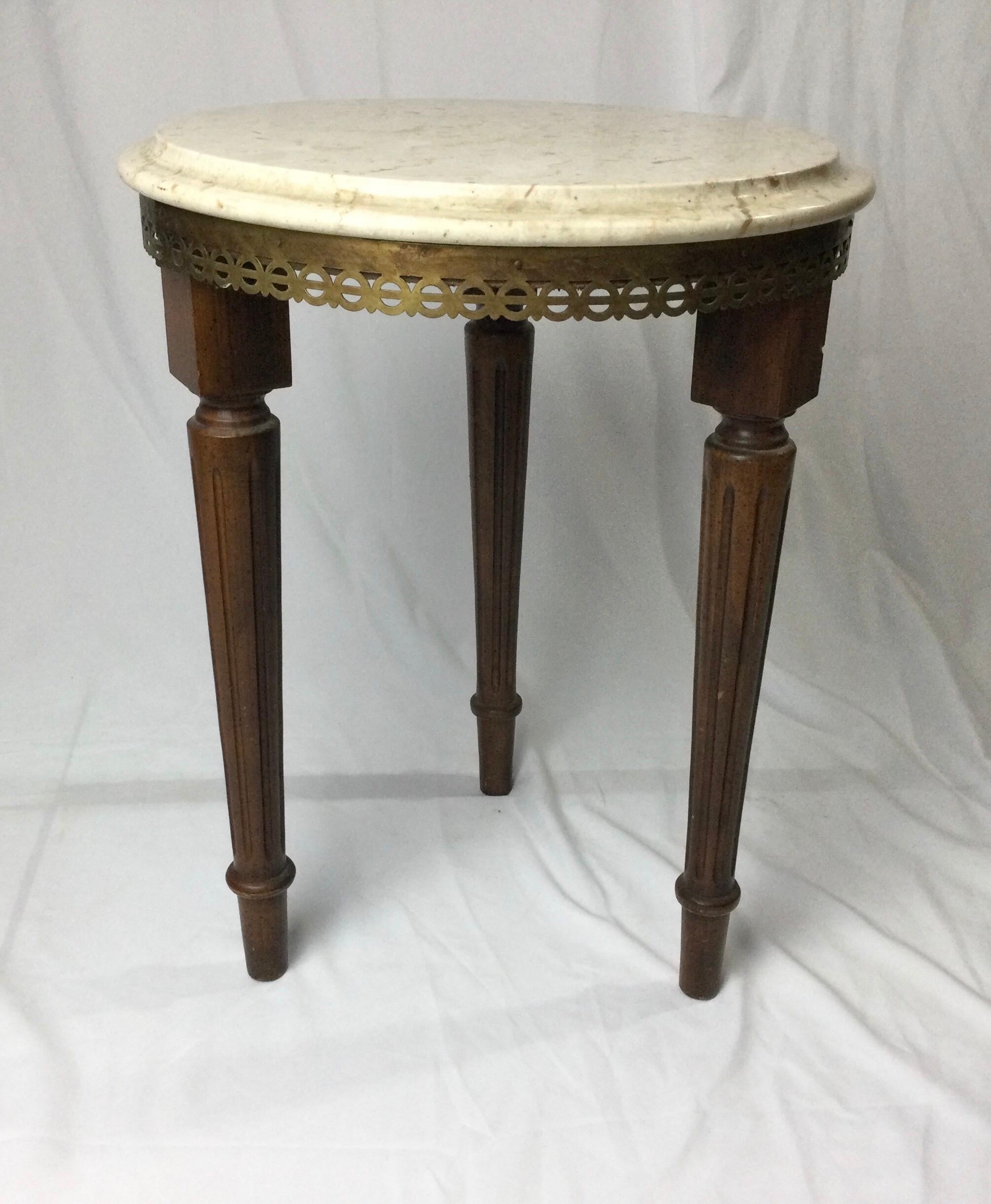 Wonderful little drink stand or plant stand with marble top. 14” in diameter and 18” tall. Dark brass trim above fluted tapered legs. Age appropriate wear. Tinny flea bite to the edge of marble.