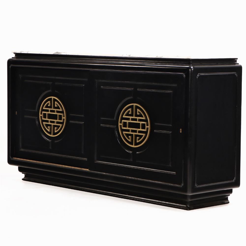Un'imponente credenza di metà secolo, realizzata in Argentina intorno al 1950, caratterizzata da un'audace finitura ebanizzata, un lussuoso piano in marmo bianco venato e raffinati supporti in bronzo. Alla maniera di James Mont, il pezzo presenta la