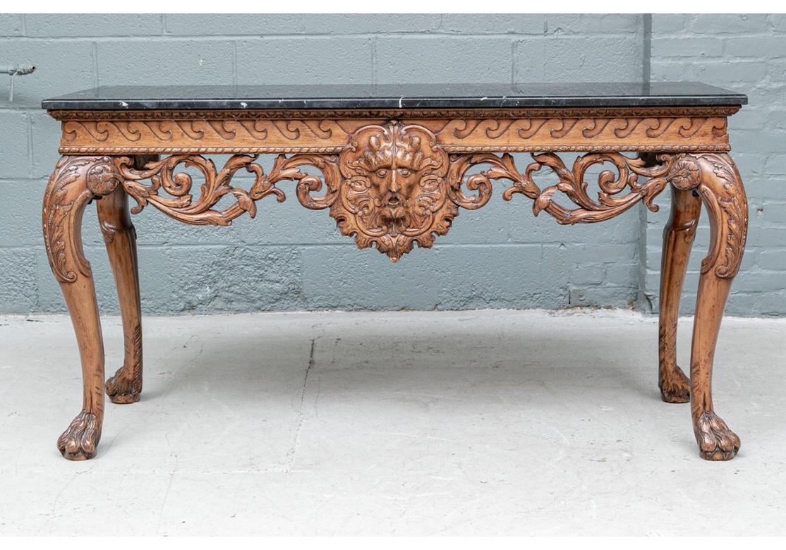 A strongly carved and impressive Georgian Style Console. The black marble topped table in a walnut finish with a running wave frieze over deep open foliate scrolled bands on all sides. The front with a center carved monstrous mask. Raised on heavy