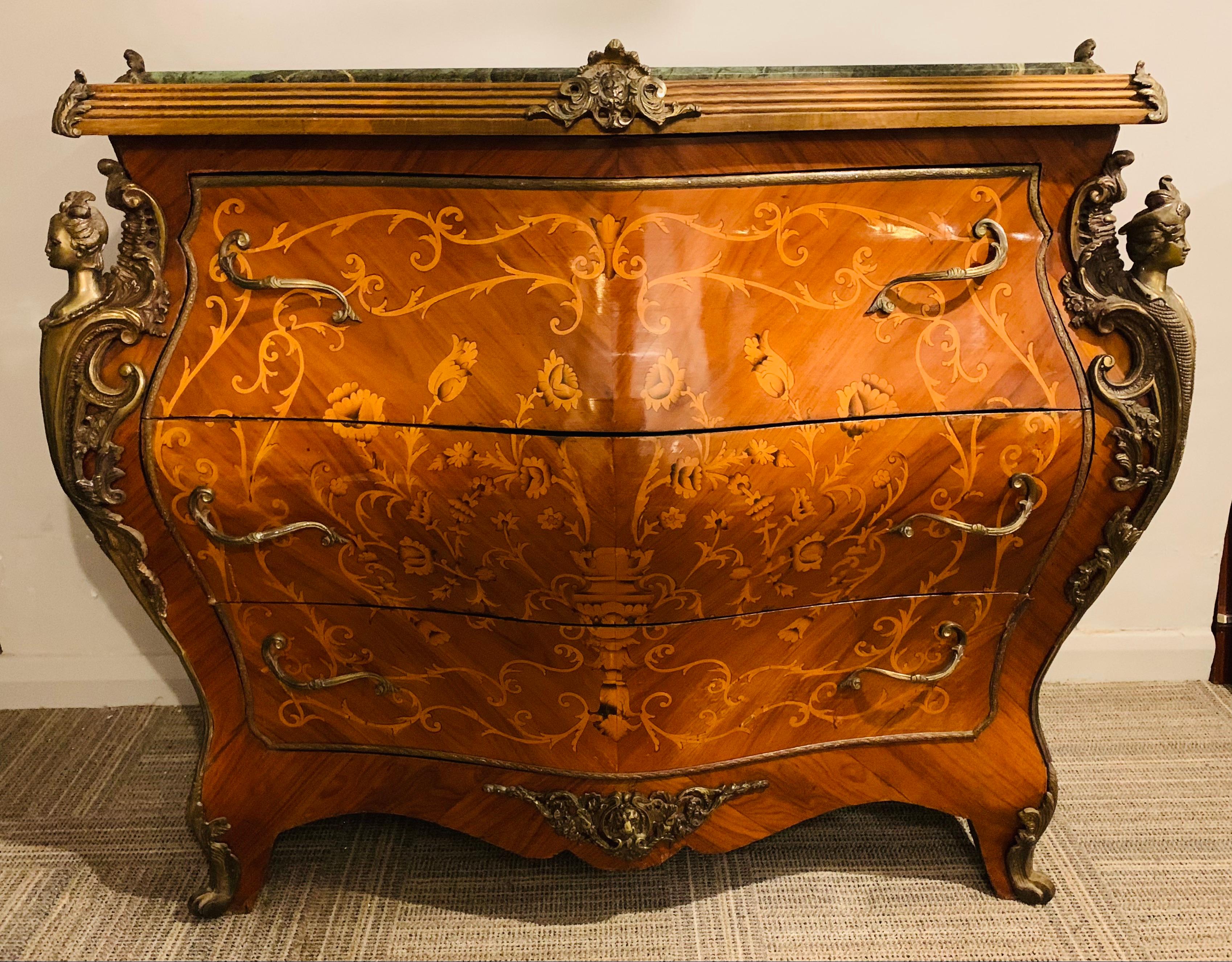 A beautiful French Louis XV style bombe chest with a contoured and beveled green marble-top, three-drawers with detailed ornate parquetry inlay dating from around the early to mid 20th century. The shapely three contoured drawers of varying sizes