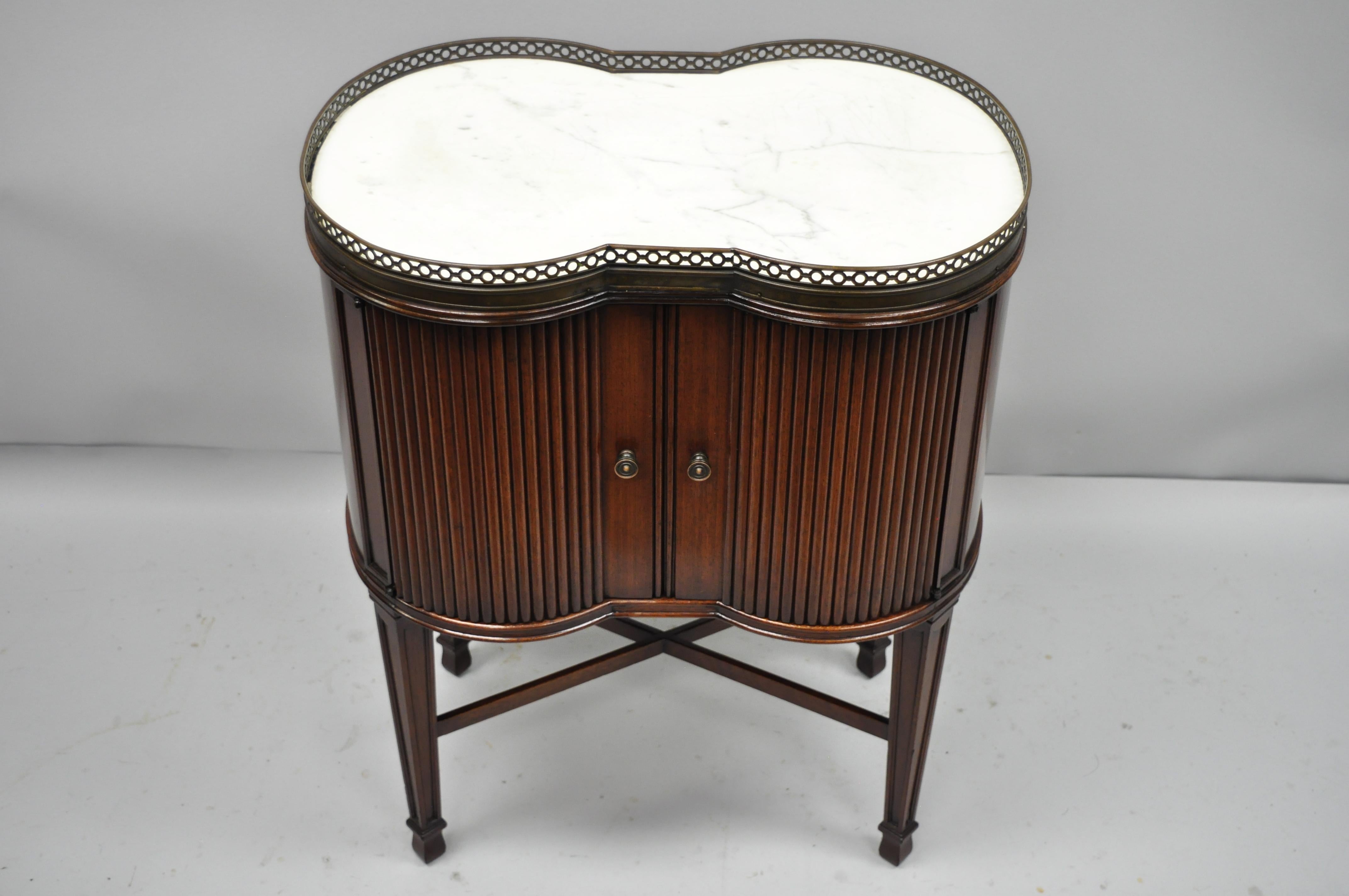 Marble-Top French Louis XVI Maison Jansen style bombe side table. Item features shapely bombe form, inset white shaped marble top, 2 swing doors, tapered legs, stretcher support, and pierced brass gallery, circa 1940. Measurements: 29