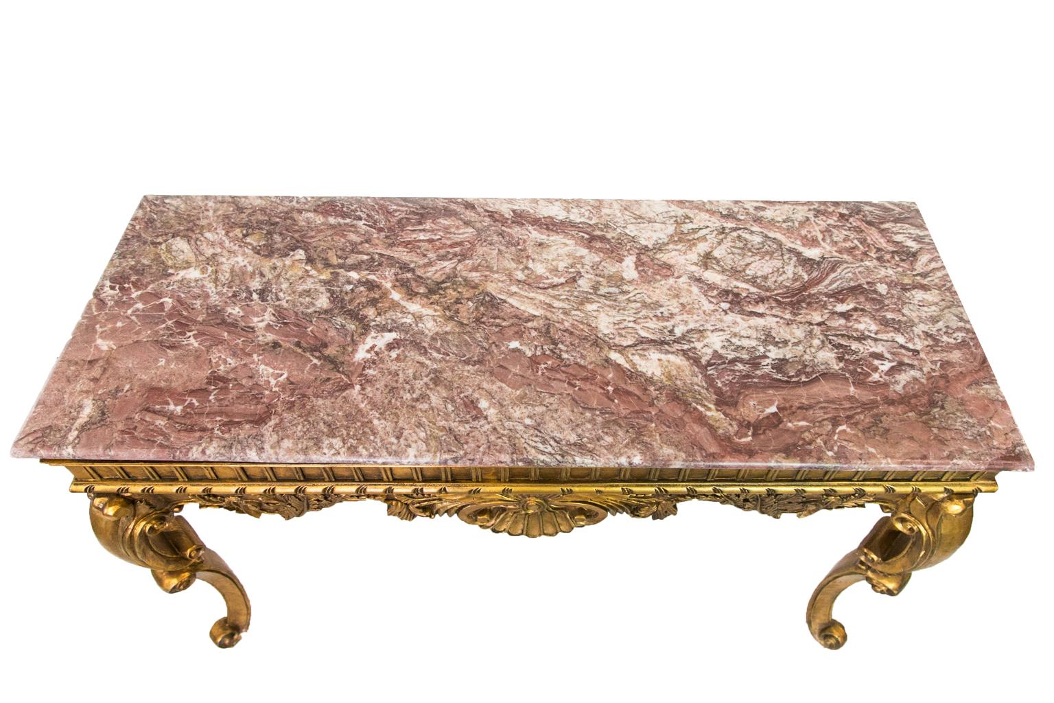 This marble top gold console table is finished on all four sides. The frieze has carved moldings and legs carved with reversing volutes.