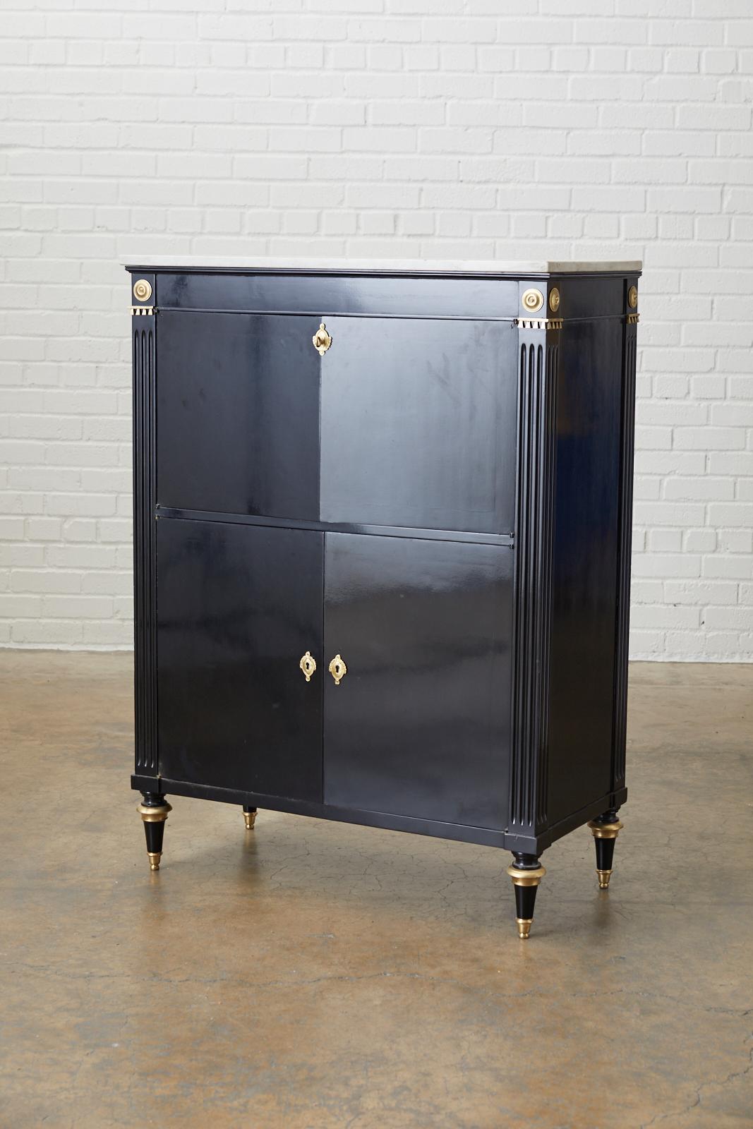 Fantastic neoclassical directoire style dry bar cabinet by Maison Jansen. Features an ebonized mahogany case having a Carrara marble top. The case is decorated with bronze embellishments and reeded column style corners. The top opens to a glass