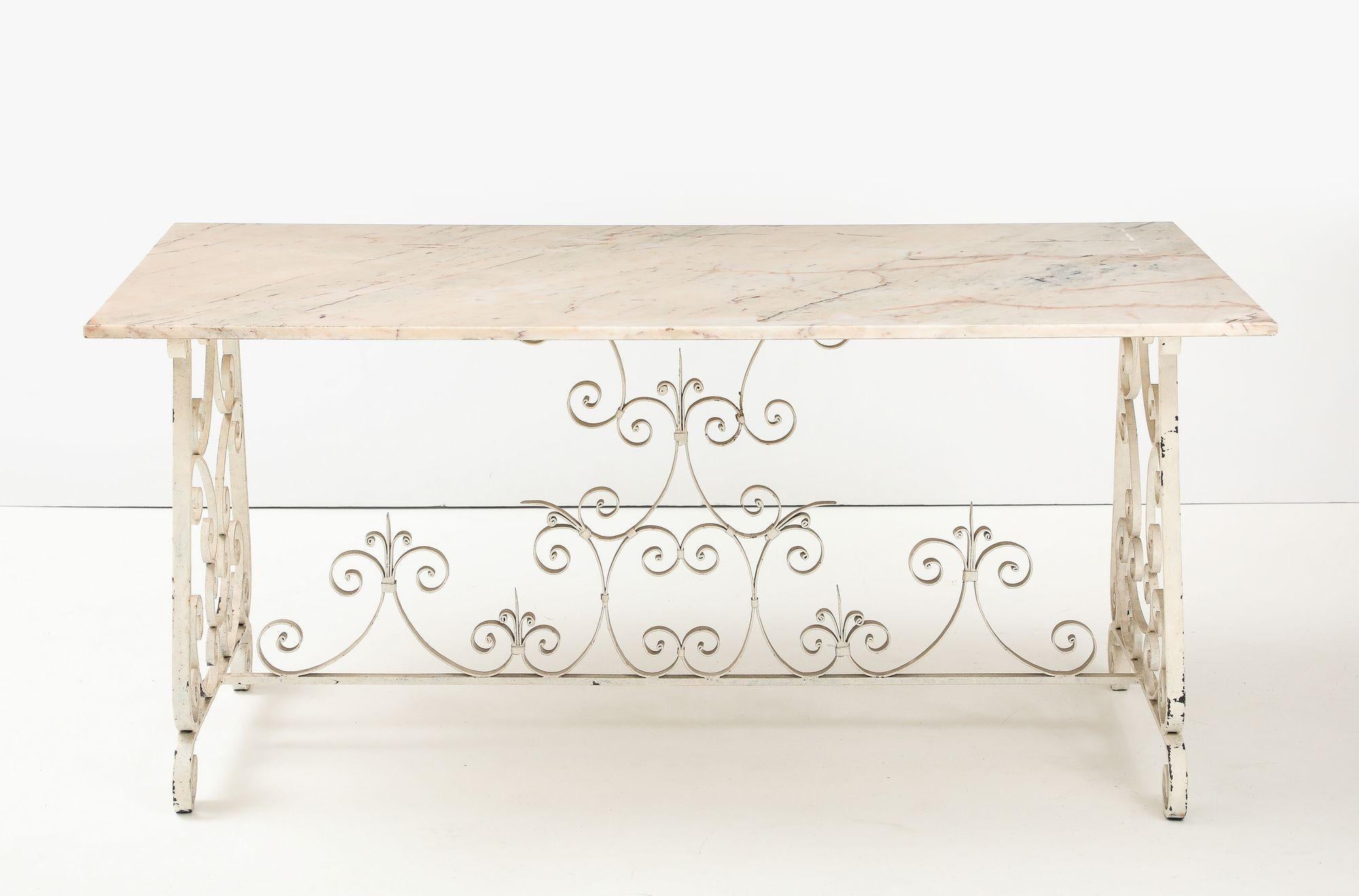 Elegante y atemporal, esta mesa de comedor inglesa presenta un tablero de mármol en tono marfil con vetas rosadas, bellamente combinado con una base de metal con volutas pintada en blanco clásico. Fabricada en Inglaterra a mediados del siglo XX, la
