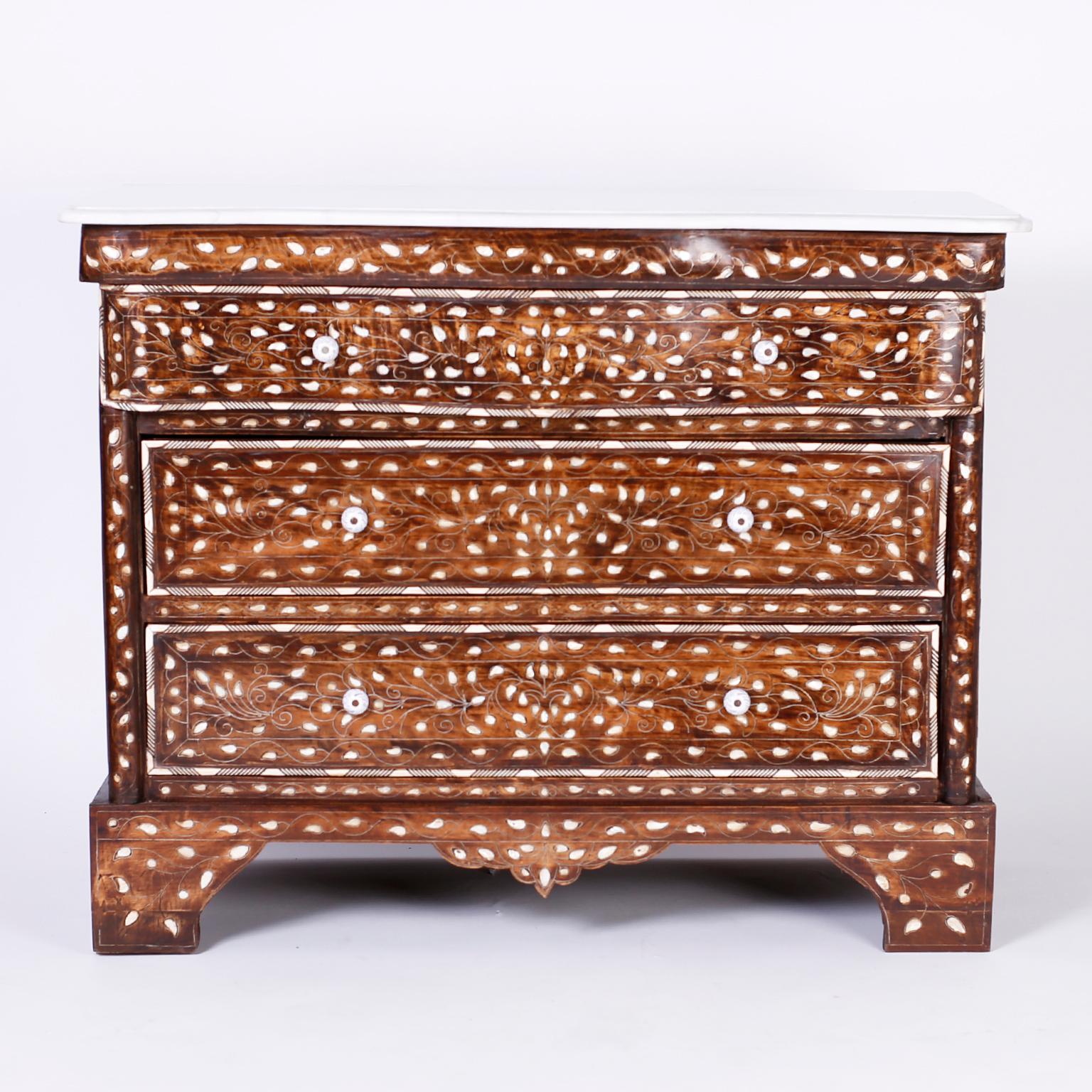 Three drawer chest or commode featuring a white marble top, serpentine top drawer, geometric bone borders, mother of pearl floral inlays connected by delicate painted vines, paneled sides, and classic bracket feet. 