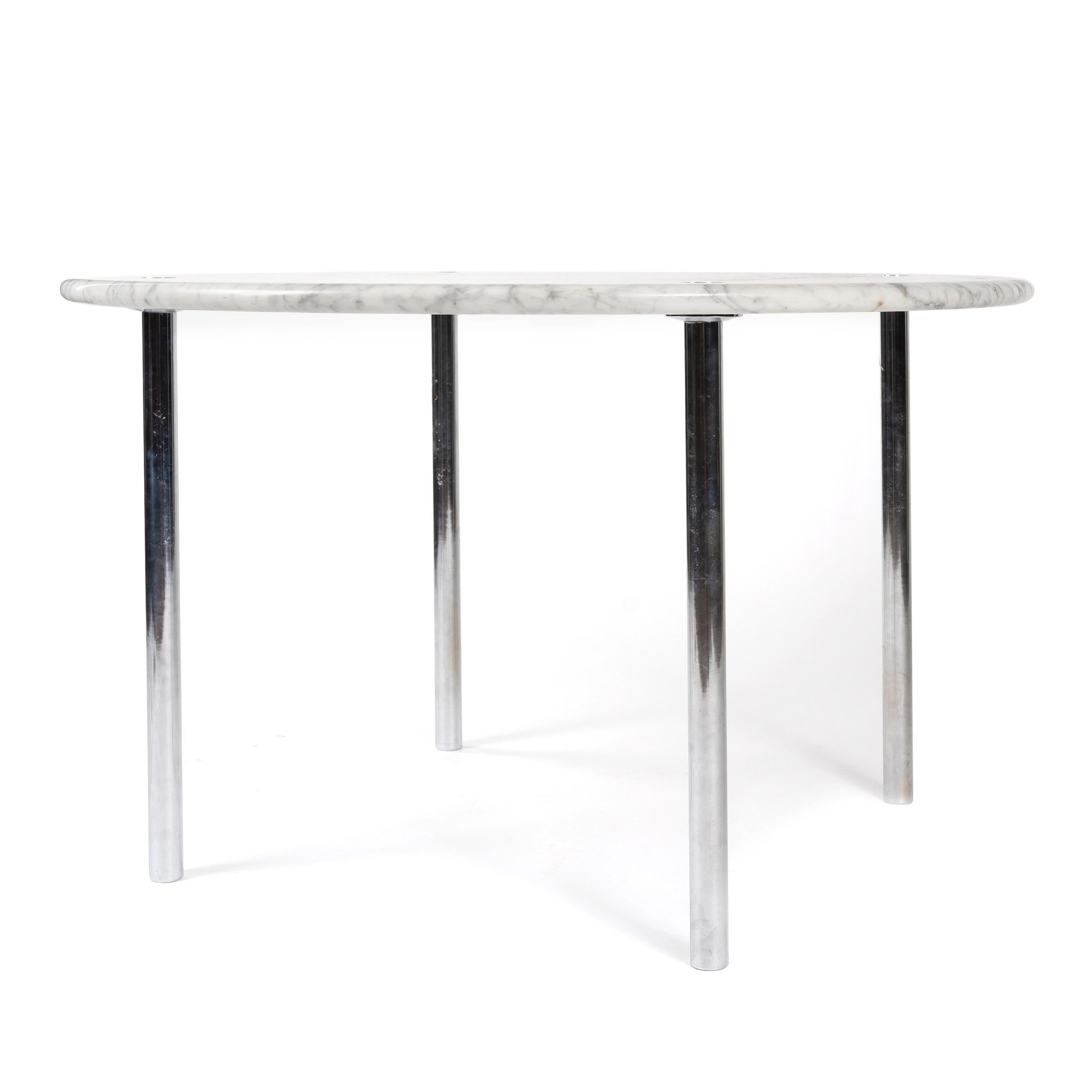 A circular dining table with a marble top with a bullnose edge on 'through-tenon' chrome cylinder legs.