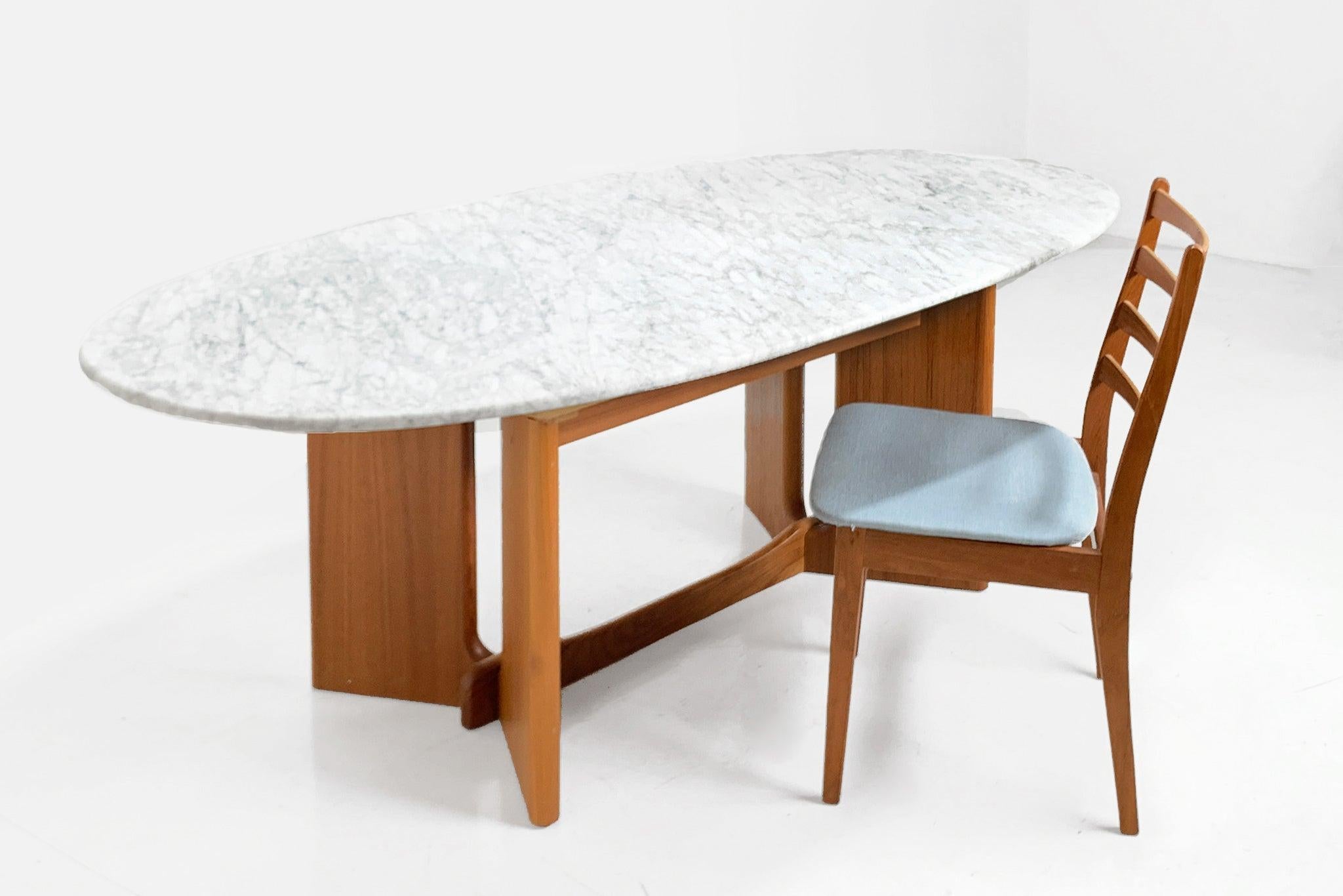 A classic Mid-Century Modern dining table with a teakwood base supports a gorgeous oval slab of Carrara marble. It's the perfect blend of style and substance, whether you're hosting a formal dinner or a casual brunch, its spacious oval shape