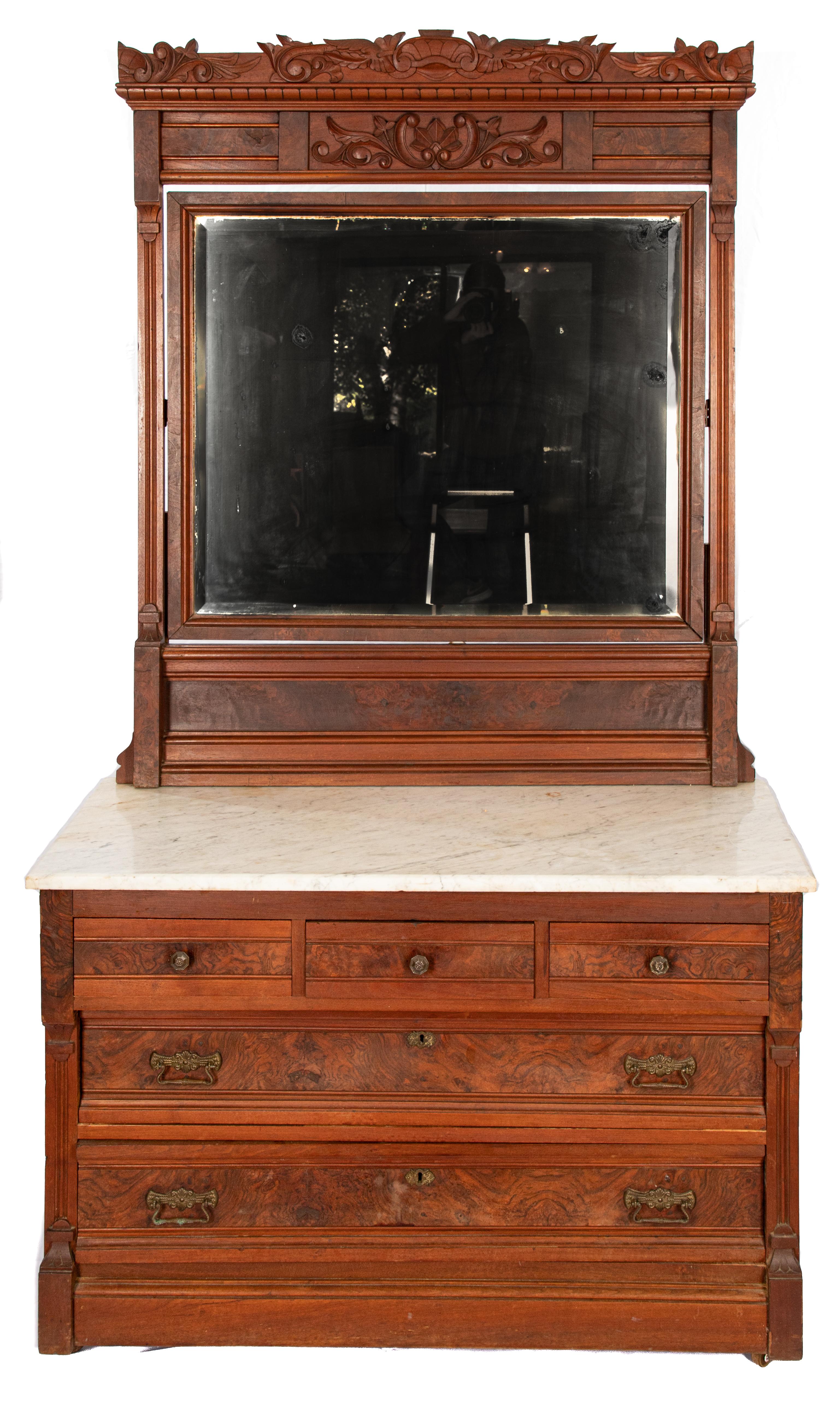 Offering this walnut marble-top dresser. The dresser is 3 drawers over 2 long drawers. The marble is a white marble top with an attached mirror. The mirror tilts and has a hand carved frame.