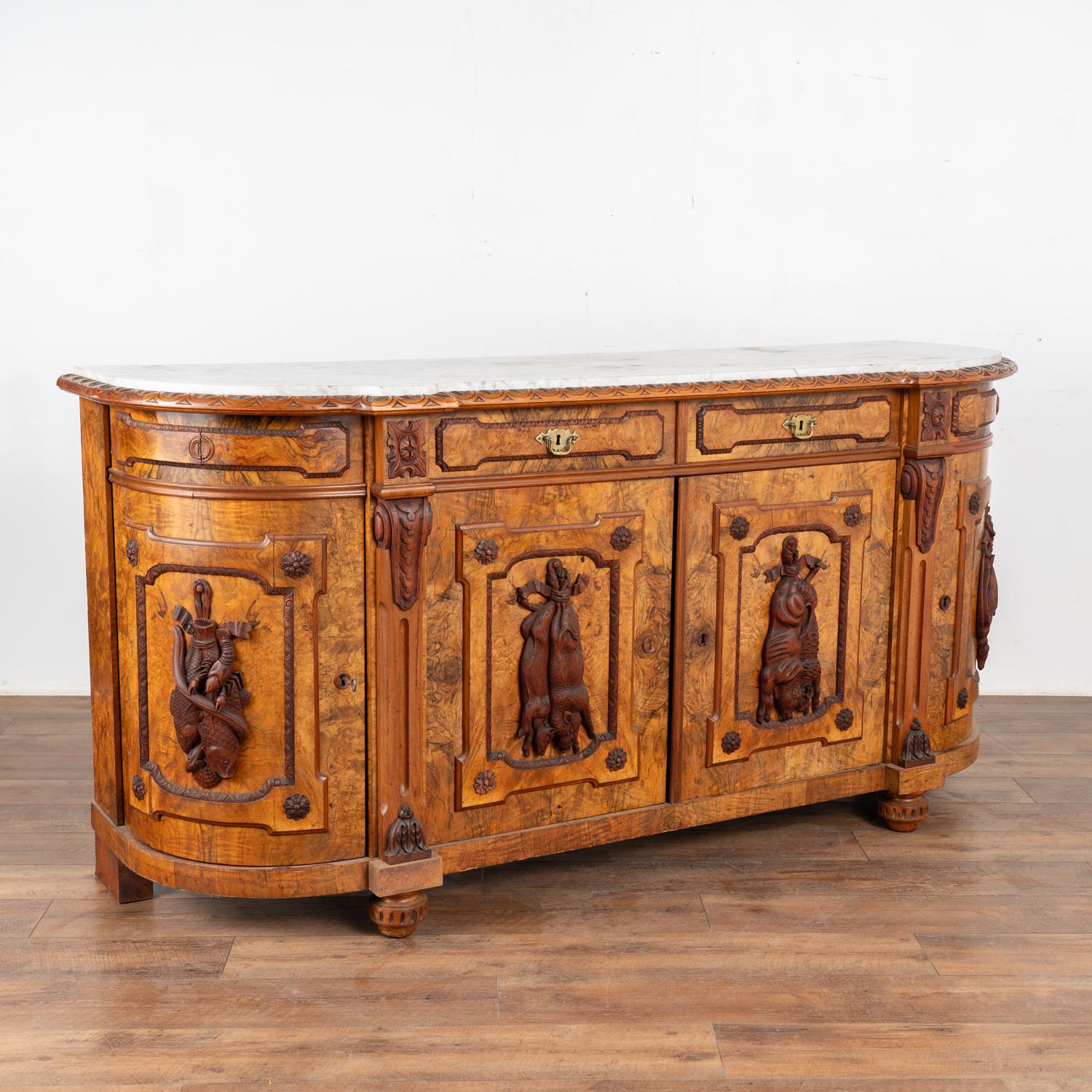Stunning walnut sideboard with original marble top. Note the striking burled wood and curved cabinet ends.
Examine close up photos to appreciate the applied Black Forest hunt carvings including fish, boar, ram and fowl on each door.
Interior