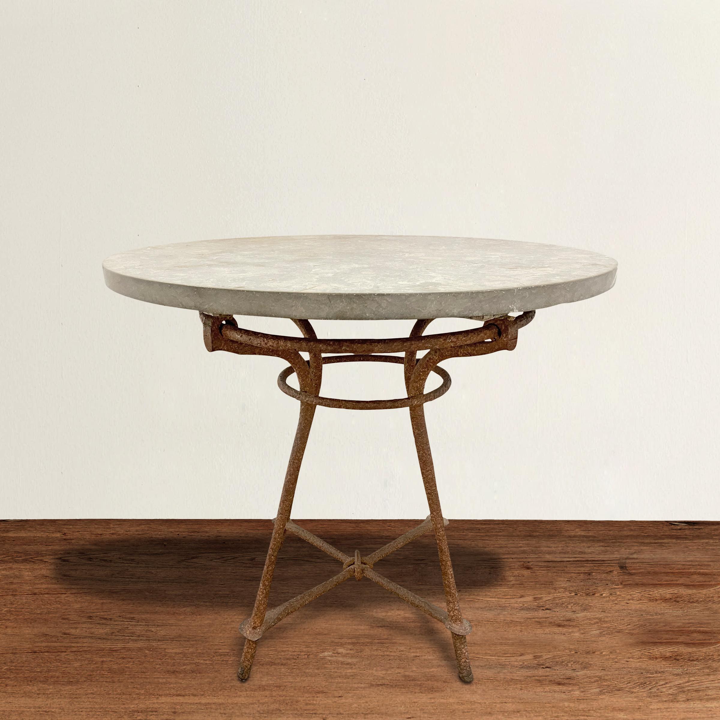 A strong yet charming early 20th century American café table with a Giacometti-inspired hand-wrought iron base with a knot connecting the crossbars, and a thick gray marble top. The table is a wonderful size for a small breakfast table, side table