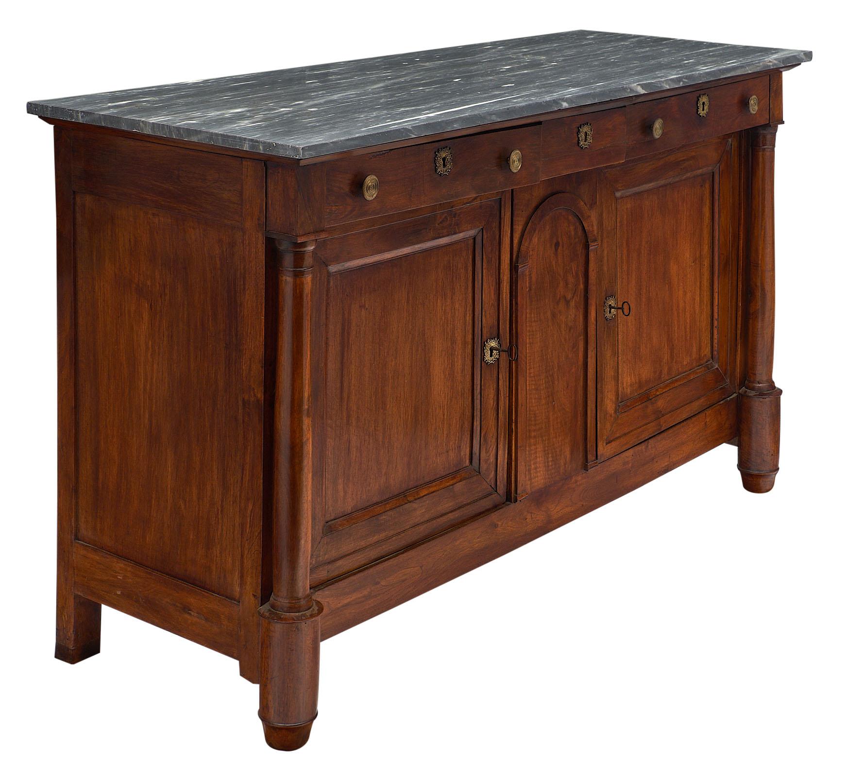 Empire period “grand buffet” of solid walnut, waxed and patinated. Fully restored, this important credenza features two doors, three dovetailed drawers and a “Turquin” marble top. We loved the fine craftsmanship, detached columns and original bronze