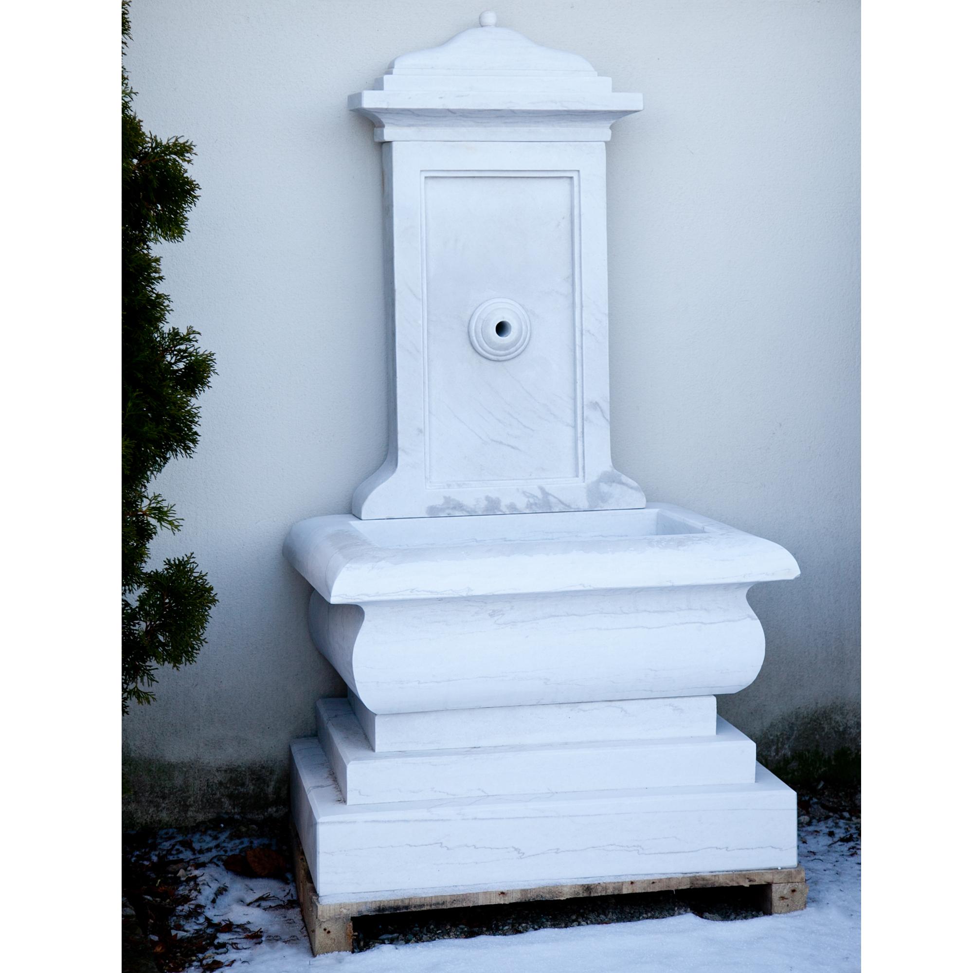 Wandbrunnen aus handgeschnitztem weißem Marmor mit gestuftem Sockel, profiliertem Becken und hoher Rückwand.