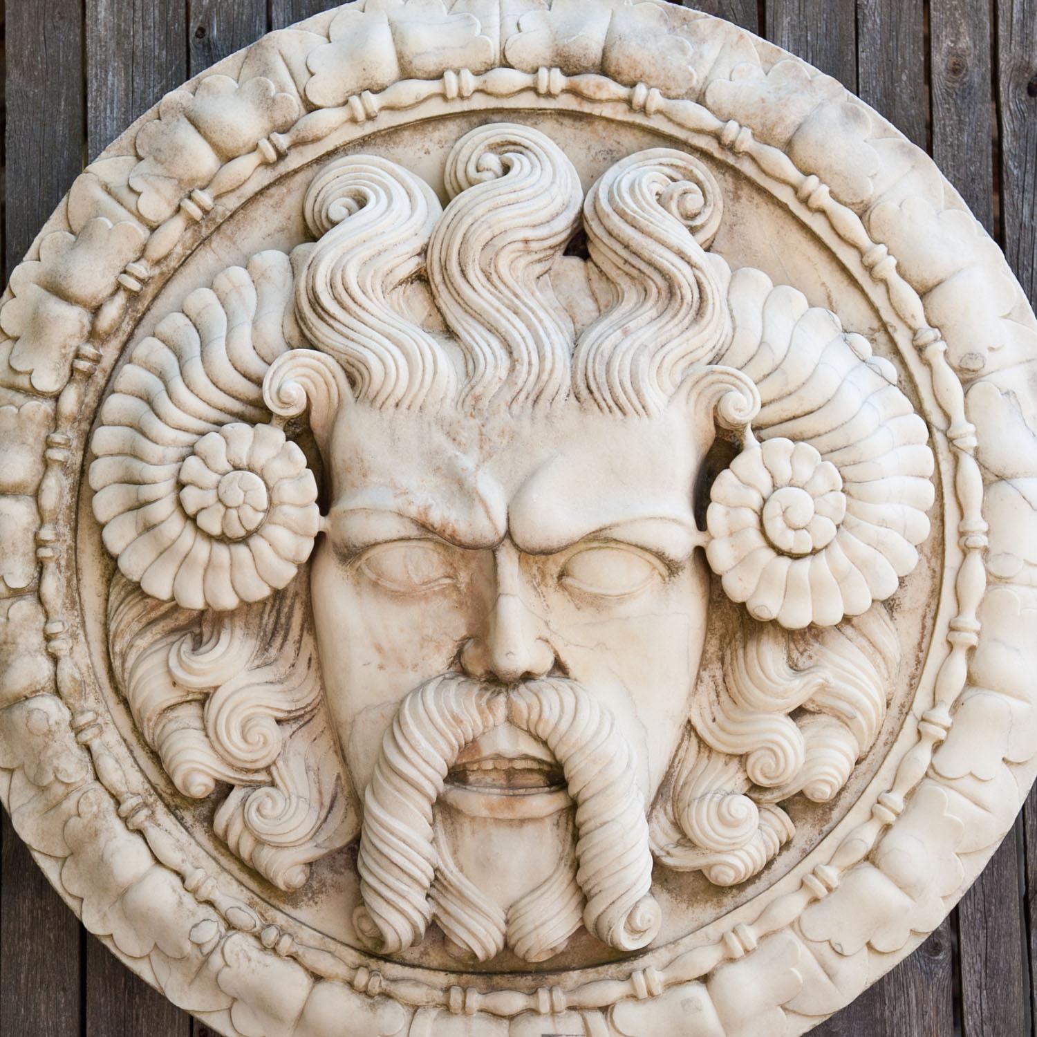 Large round marble wall relief with a leaf decorated boarder and a very expressive male mascaron with ram’s horns and a curly beard and hair.