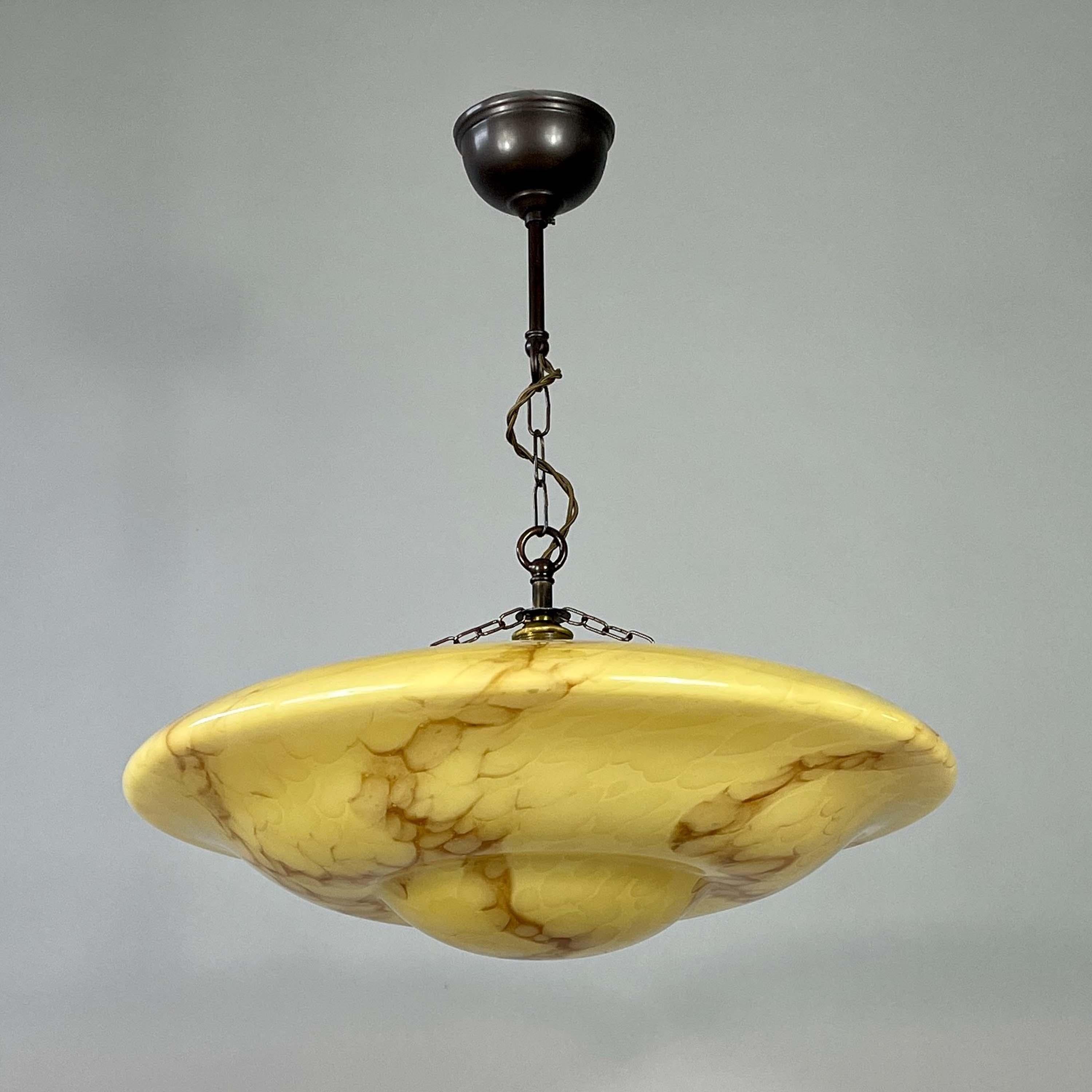 Questo ciondolo Art Déco è stato progettato e prodotto in Germania tra gli anni '30 e '40 del secolo scorso. 

La lampada è caratterizzata da un paralume scultoreo in vetro marmorizzato color sabbia.  con calde venature marroni, formando una