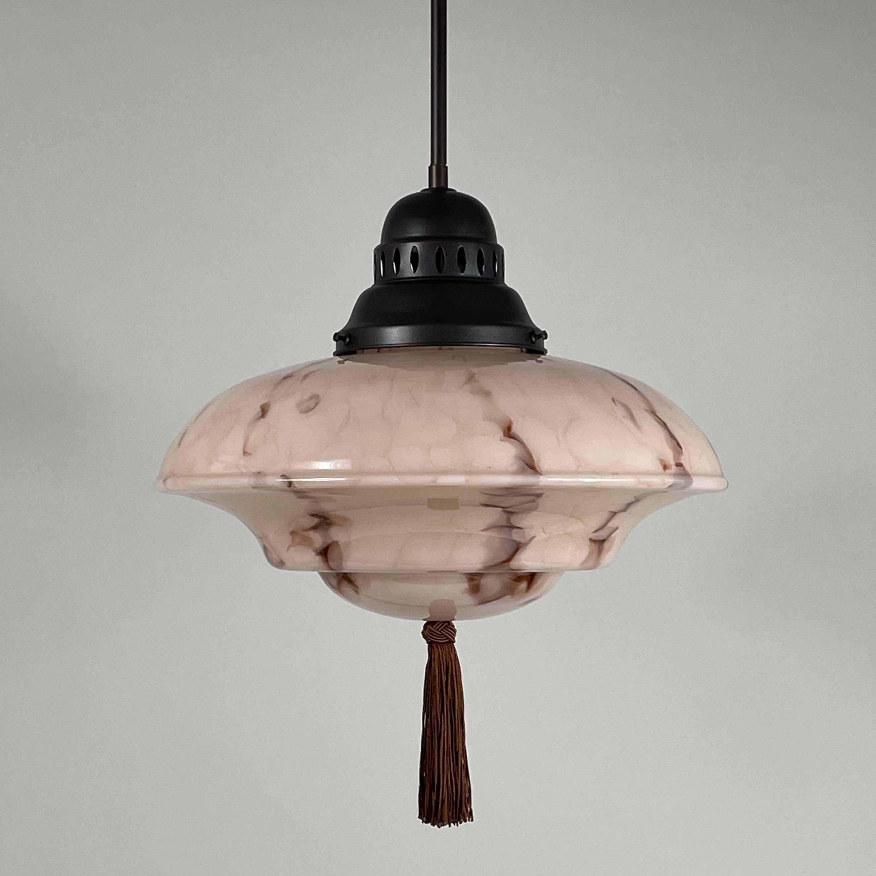 This elegant pendant was designed and manufactured in Germany during the Bauhaus Period in the 1920s to 1930s.

It features a pale rose colored opaline glass lampshade with brown and beige marbled decor, bronzed / burnished metal hardware and dark