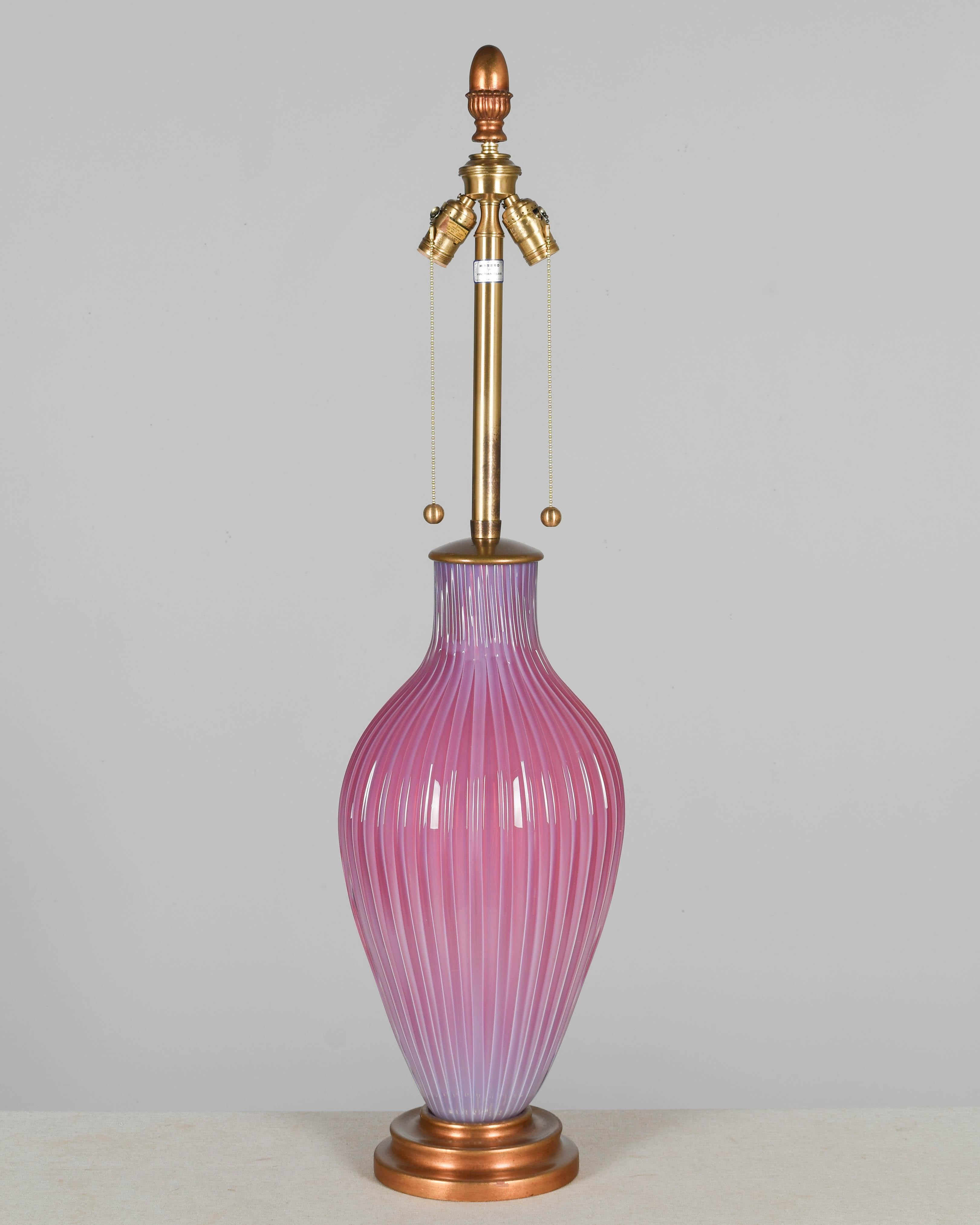 A Mid Century Murano glass lamp by Seguso, imported by The Marbro Lamp Company. Hand-blown opalescent pink cased glass with thick ribbed form and nice proportions. Double socket with pull chains. Large gilded acorn finial. Wood base with warm gilt