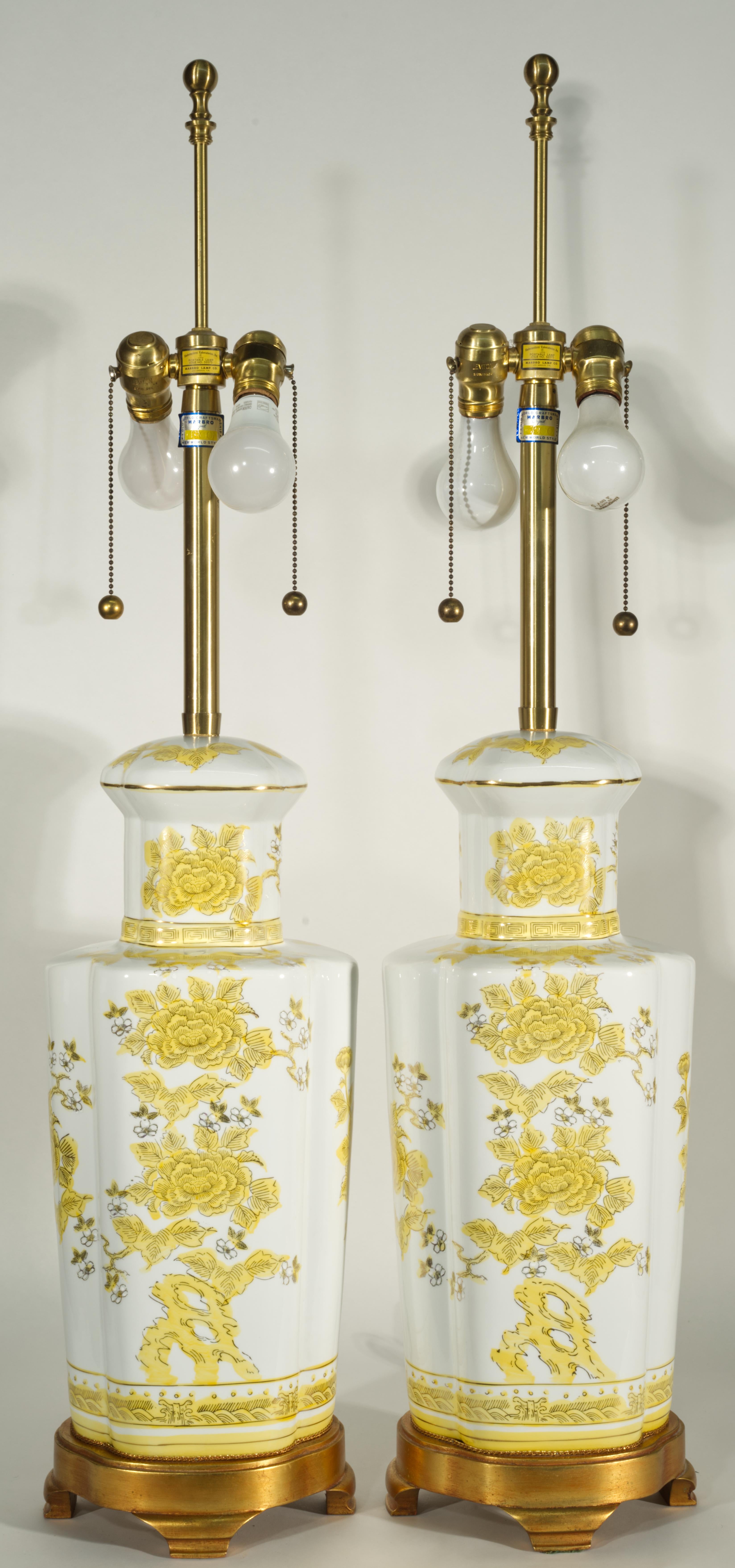 Vintage pair of Chinoiserie porcelain urn table lamps by The Marbro Lamp Company features hand-painted, highly detailed Imari style decor in bright, cheerful yellow color with gold accents on white background. The lamps are mounted on carved and