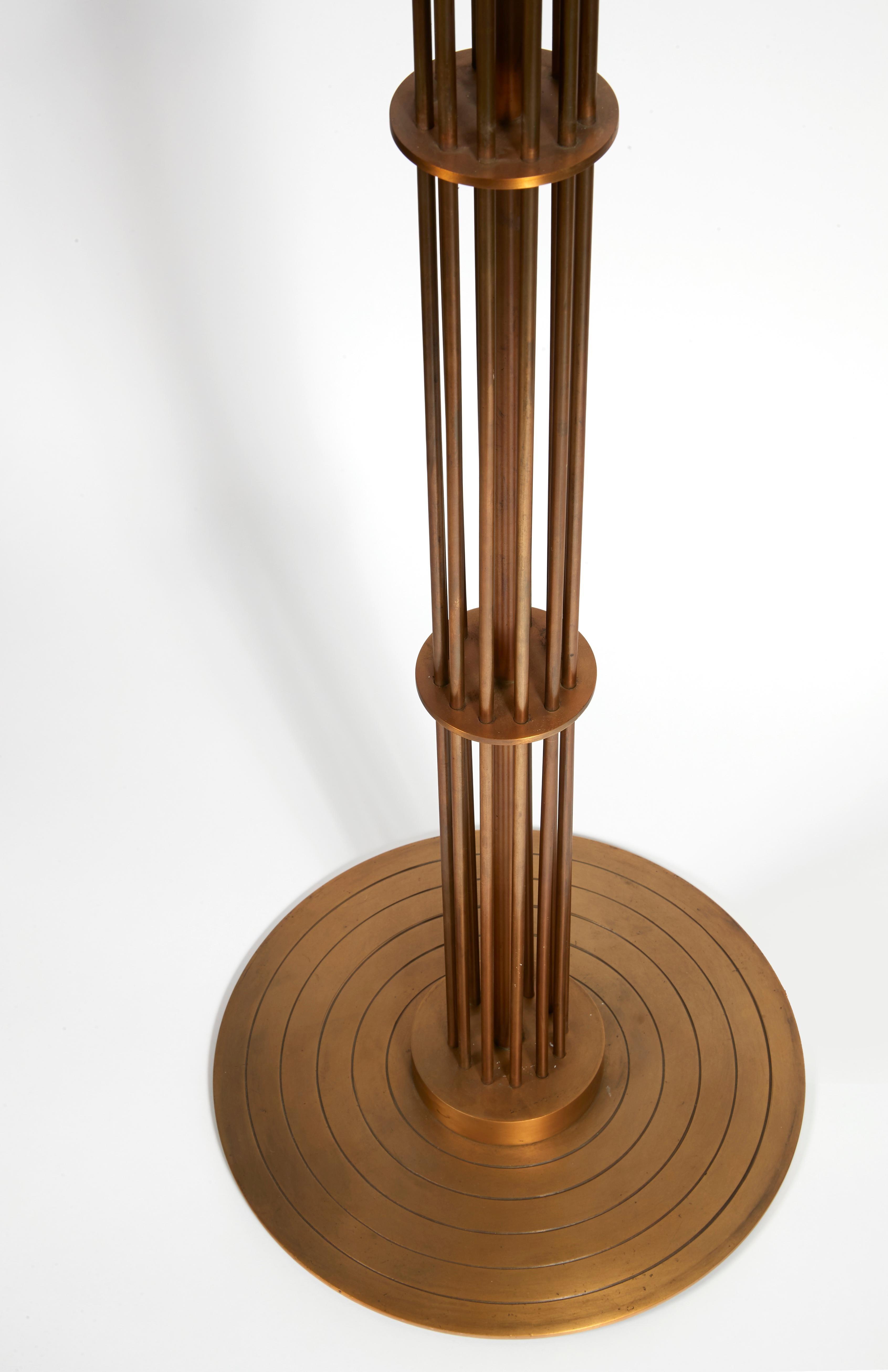 Avec une base en laiton patiné composée de tubes formant une cage cylindrique sur une base circulaire plate rainurée.