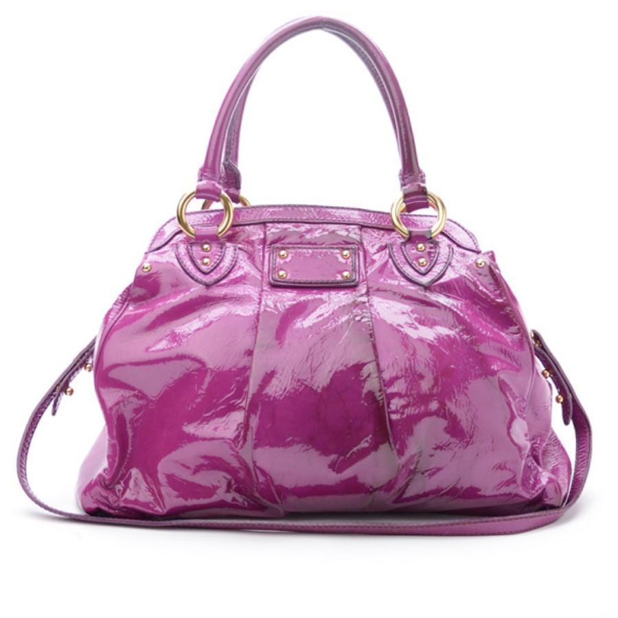 Eye catching and simple, this Marc Jacobs Alyona Satchel will have all eyes on you! Made from shiny patent leather, it features a push lock detailing on front, two rolled handles, pleat detailing from the center and a detachable shoulder strap. The