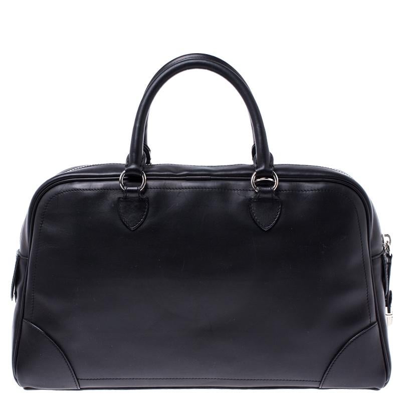 Crafted from black leather, this dome satchel by Marc Jacobs features a smooth, well-structured exterior along with trims and a leather tag dangling to the front. It is equipped with dual top handles, protective metal feet at the bottom and a