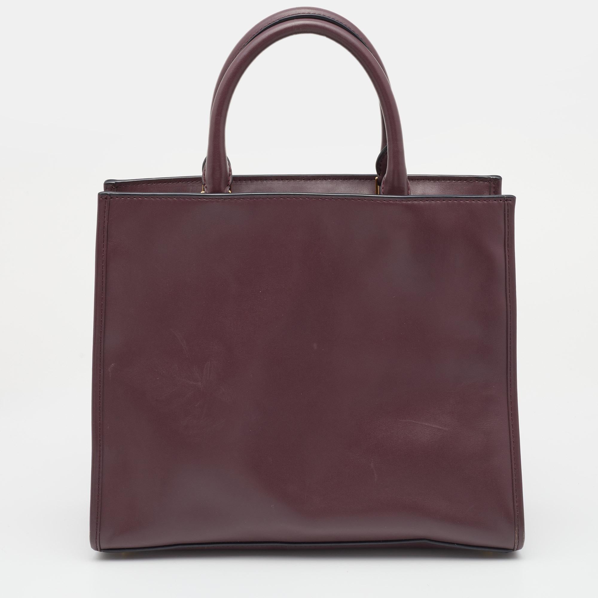 Lightweight, durable, and chic, this Marc Jacobs tote is perfect for everyday use. It features a burgundy leather body detailed with a zip pocket on the front. It opens to a spacious fabric interior. Complete with dual top handles, this