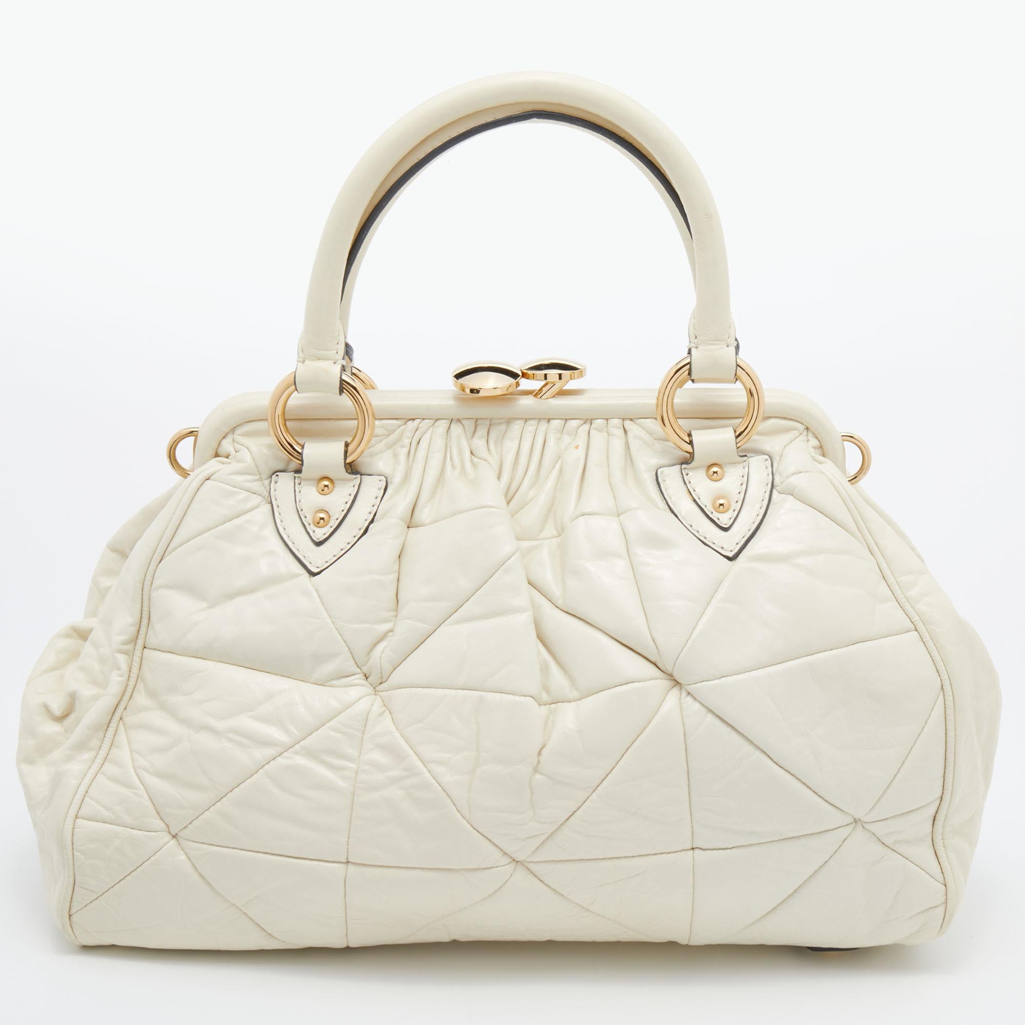This Marc Jacobs design has a cream quilted exterior crafted from leather and enhanced with gold-tone hardware. The elegant Stam bag features a kiss-lock top closure, a fabric interior, dual top handles, and a removable strap that converts this
