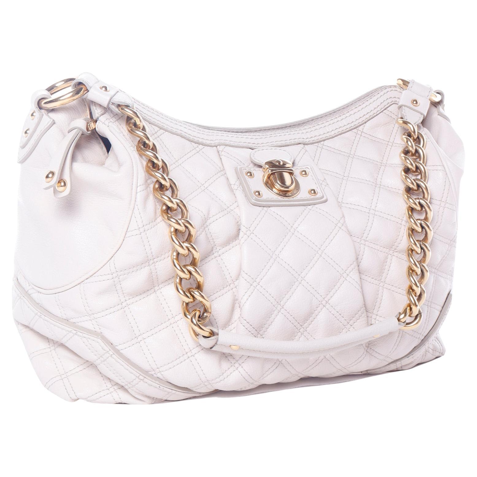 This Marc Jacobs bone quilted leather handbag has many of the designer's signature bag elements. The bag has a monogrammed zipper pull and monogrammed faux clasp hardware on the front of the bag. This variation on the hobo bag has a top zipper and a