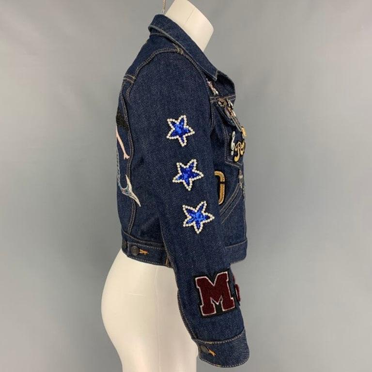 MARC JACOBS jacket comes in a indigo denim featuring a cropped style, contrast stitching, charm details, pin details, patch designs throughout, beaded details, a back embroidered sequin mermaid design, front pockets, and a buttoned