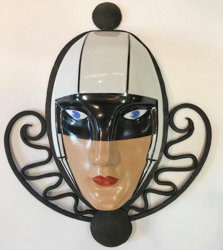 Wall mounted porcelain mask signed M. Bever Paris, Made in France, mounted in fer forge frame, circa 1925. Edgar Brandt is known to have designed wrought iron for Maison Robj, for whom Marcel Bever designed many ceramics. 

Marcel Bever was a