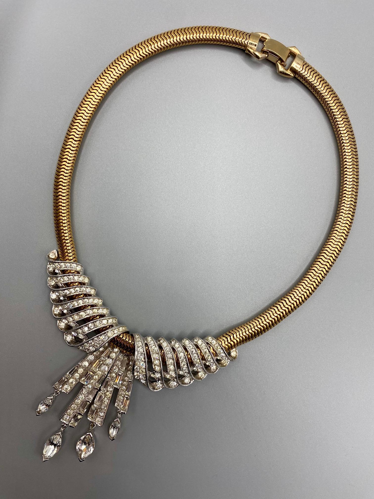 Presented is an elegant and eye catching vintage 1940s necklace by high end American fashion jewelry company Marcel Boucher. The necklace has a gold tone .25 inch wide and 15 inch long snake chain with fold over clasp in the back. The front has an