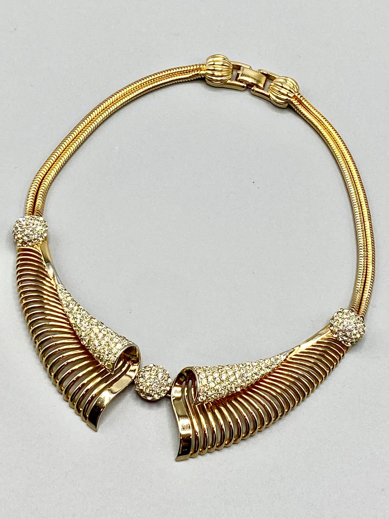 Presented is an elegant and unique vintage 1950s necklace by high end American fashion jewelry company Marcel Boucher. The necklace has a unique scroll collar design. The two sides of the bib front and the double snake chain strands are gold tone.