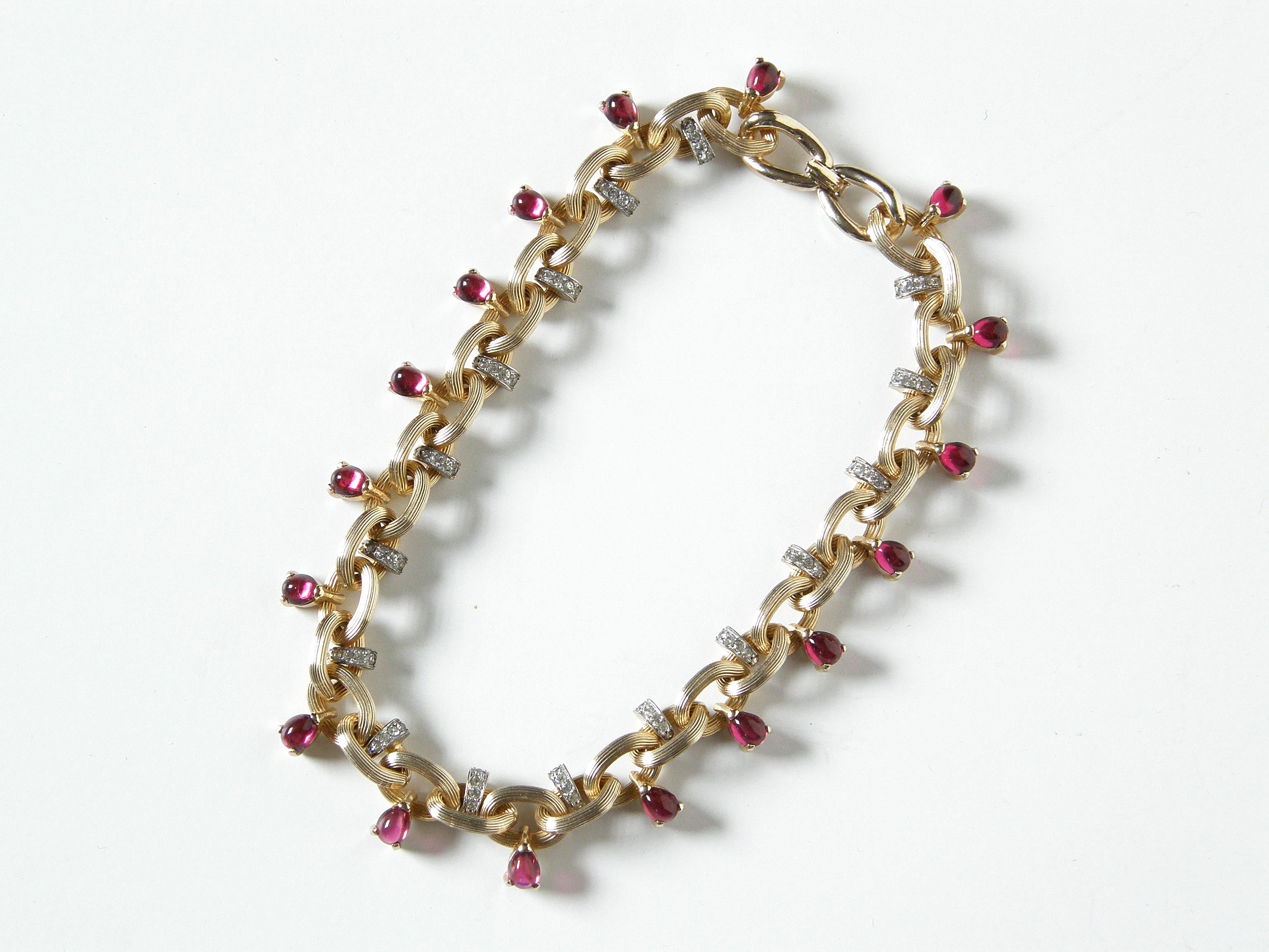 This 1950s choker necklace and matching earrings were designed by Marcel Boucher. They feature chunky, gold tone chains with a ridged texture. Alternating links of the necklace are set with either a small band of faux diamond rhinestones or a pear