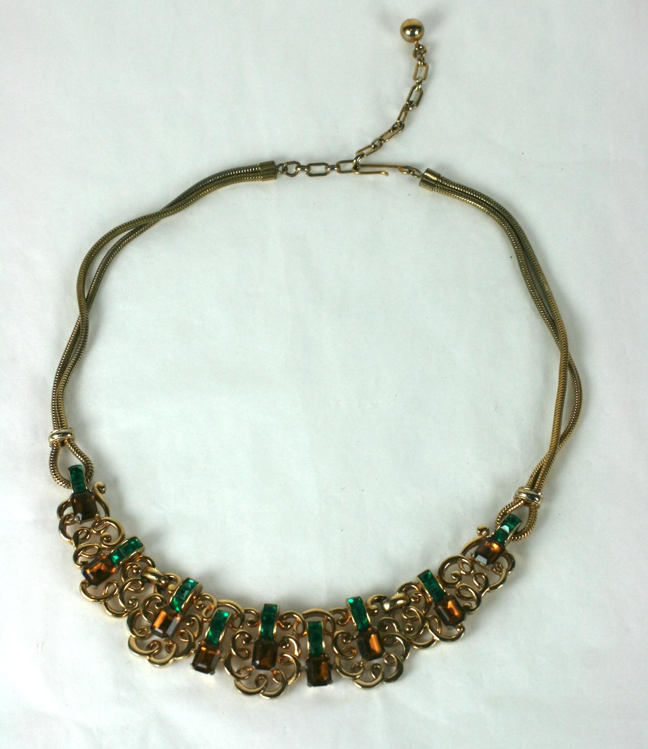 Marcel Boucher Retro-Halskette mit einem Mittelstück aus verschlungenen Mustern mit quadratisch geschliffenen Faux-Smaragd- und Topas-Pasten. Das Motiv in der Mitte wird von einer Schlangenkette mit Schlaufen gehalten.
1940er Jahre USA. Signiert