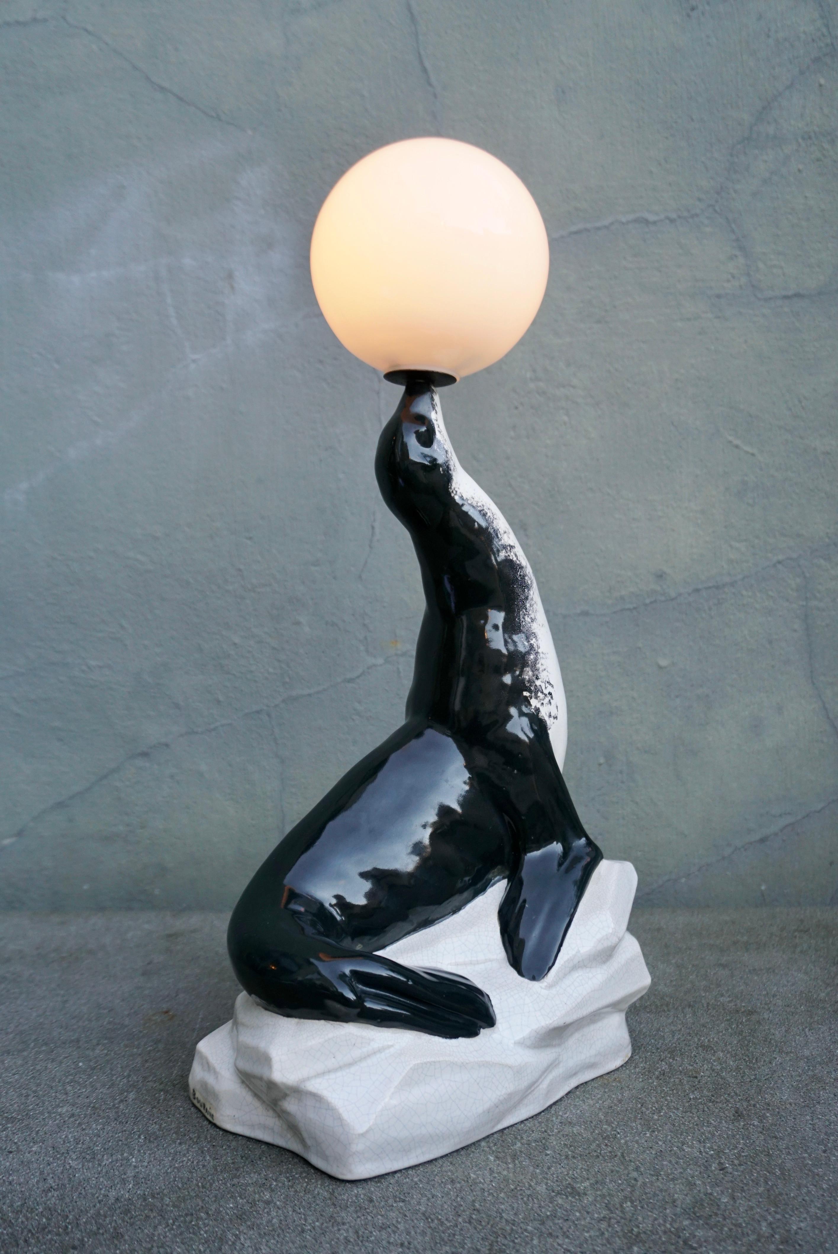 These elegant Art Deco Table lamp sculpture from Marcel-André Bouraine (1886-1948), depicts a sea lion in perfect balance holding a glass ball on its nose. 

Large rare French Art Deco sea lion juggling table lamp by Marcel Bouraine. An earthenware