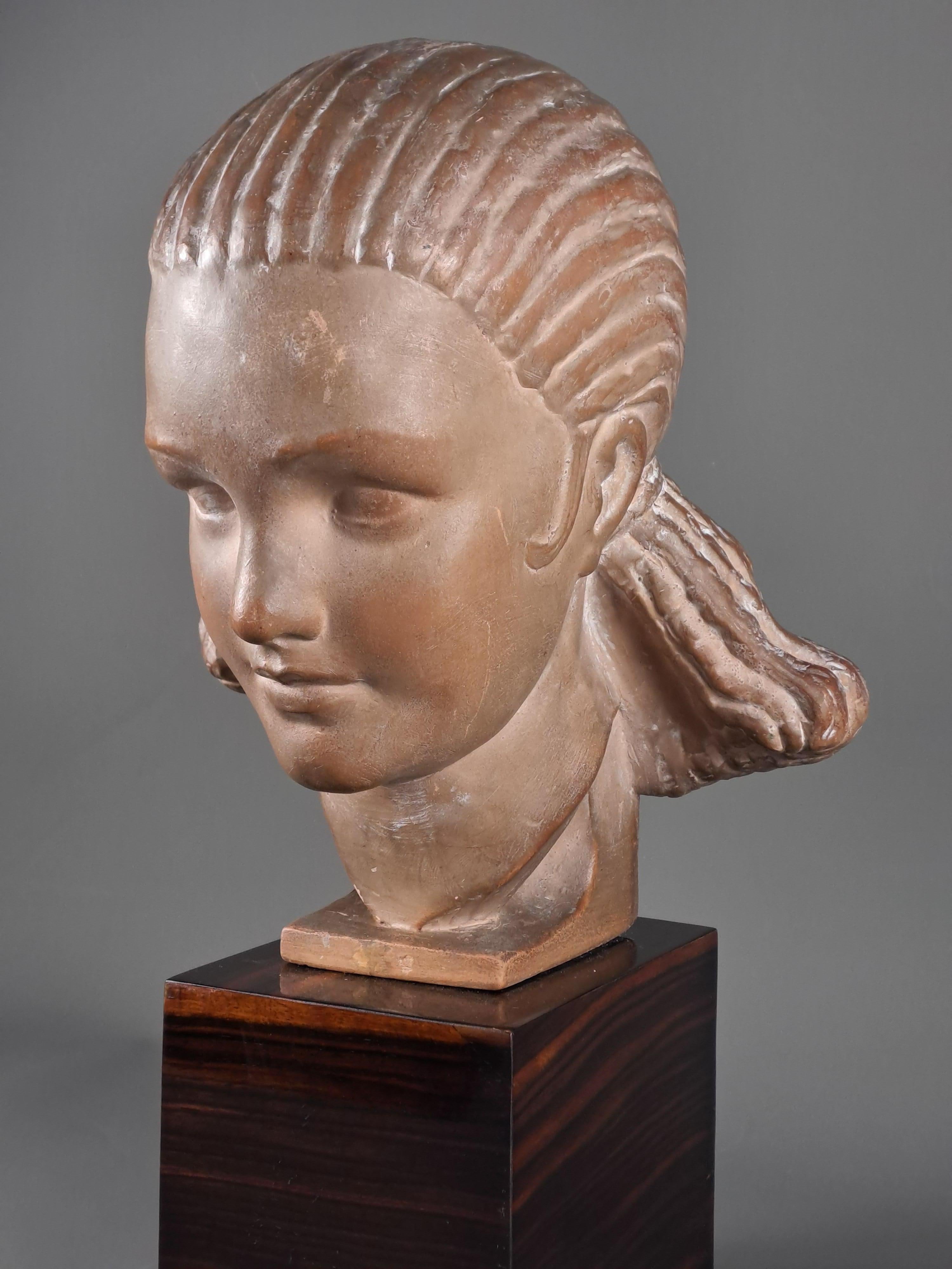 Marcel Bouraine (1886–1948)

Terracotta sculpture depicting the bust of a beautiful young woman with very fine features and a hairstyle made up of fine braids pulled back and held in a sort of large flared bun.

Art deco composition, reminiscent of