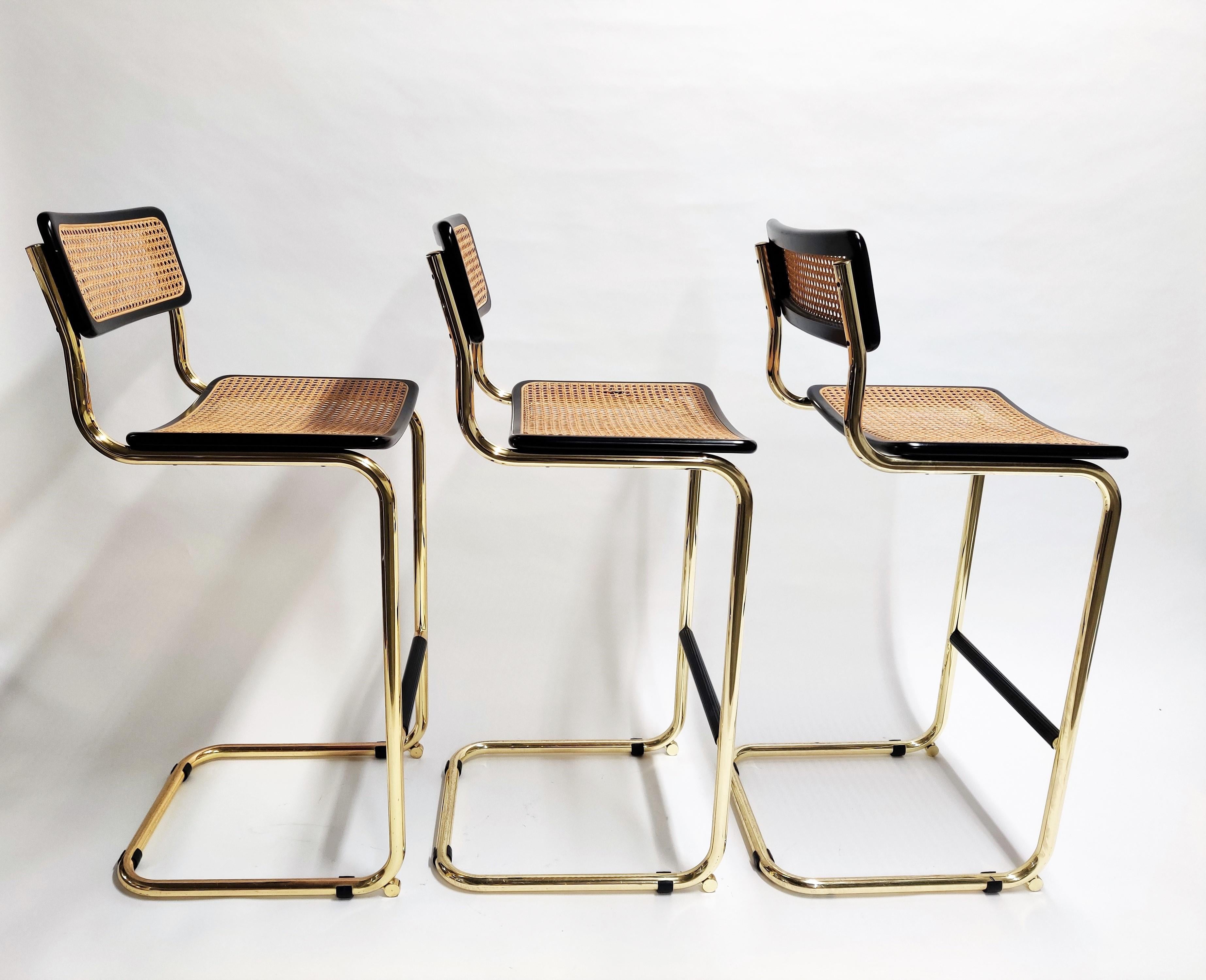 Set of 3 Marcel Breuer Bauhaus design bar stools with rare brass frames.

Tubular brass frame with cane seats and black lacquered wood, labeled 'made in italy'

All in very good condition.

Protected foot rests.

Dimensions:
Height